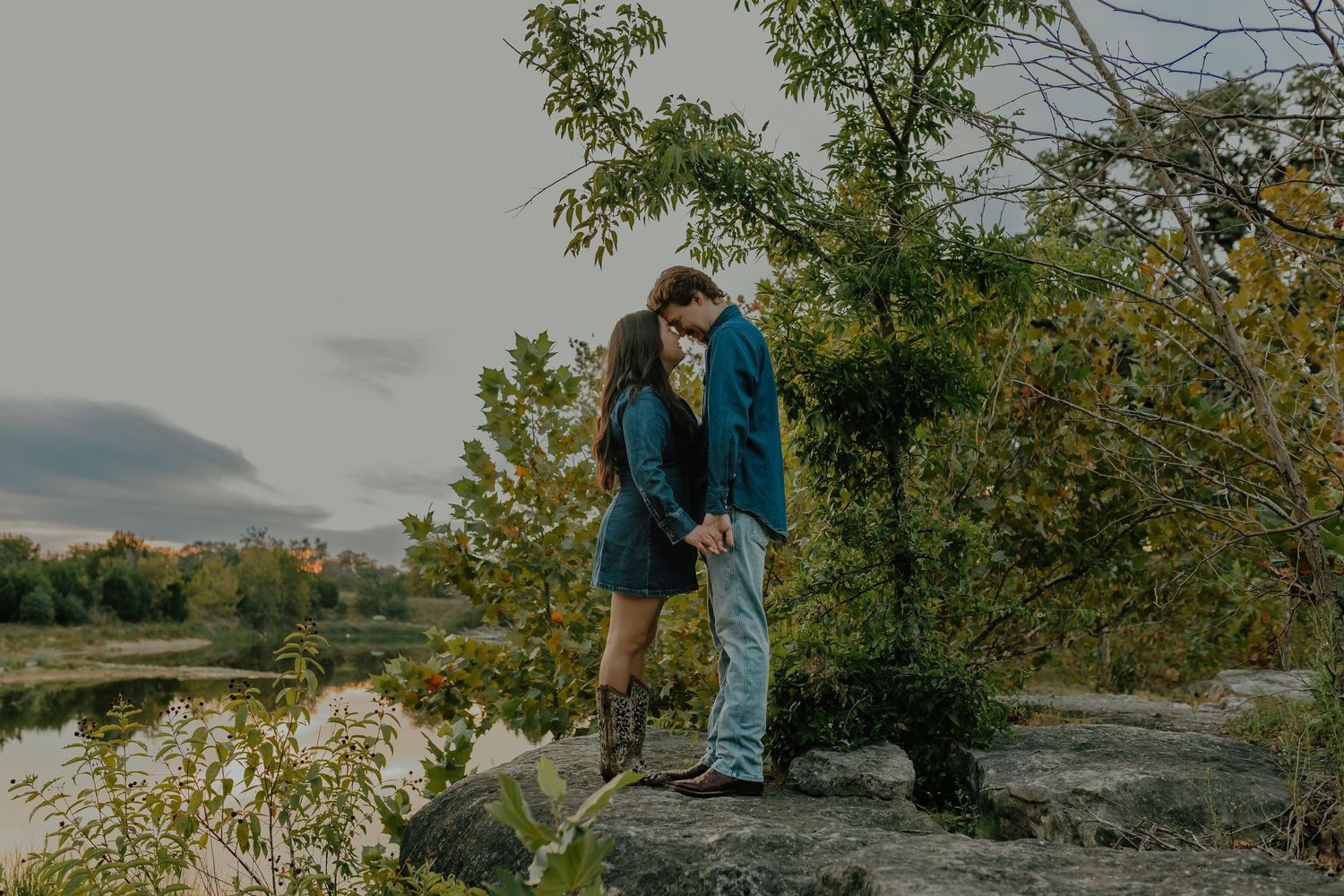 Couple stands on rocky overlook during sunset by tranquil lake.