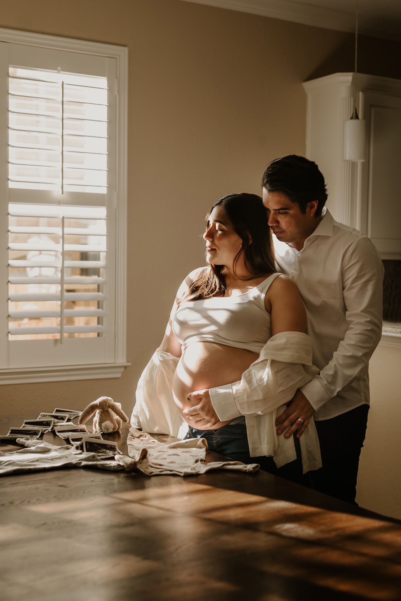Intimate maternity photo of couple by window with soft natural lighting.
