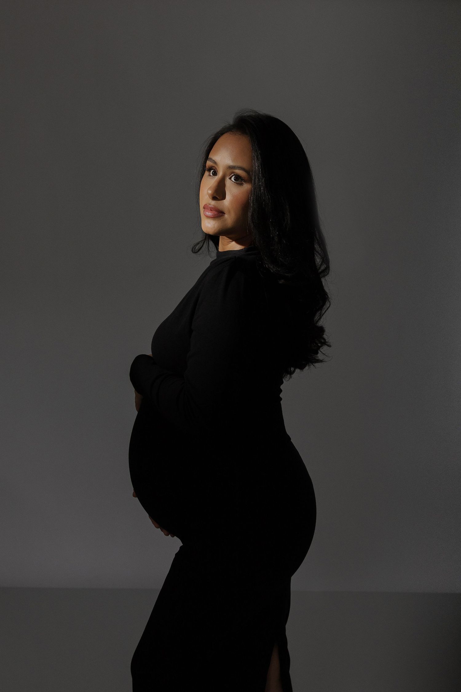 Side silhouette of an expectant mother in a black dress against a dark background.