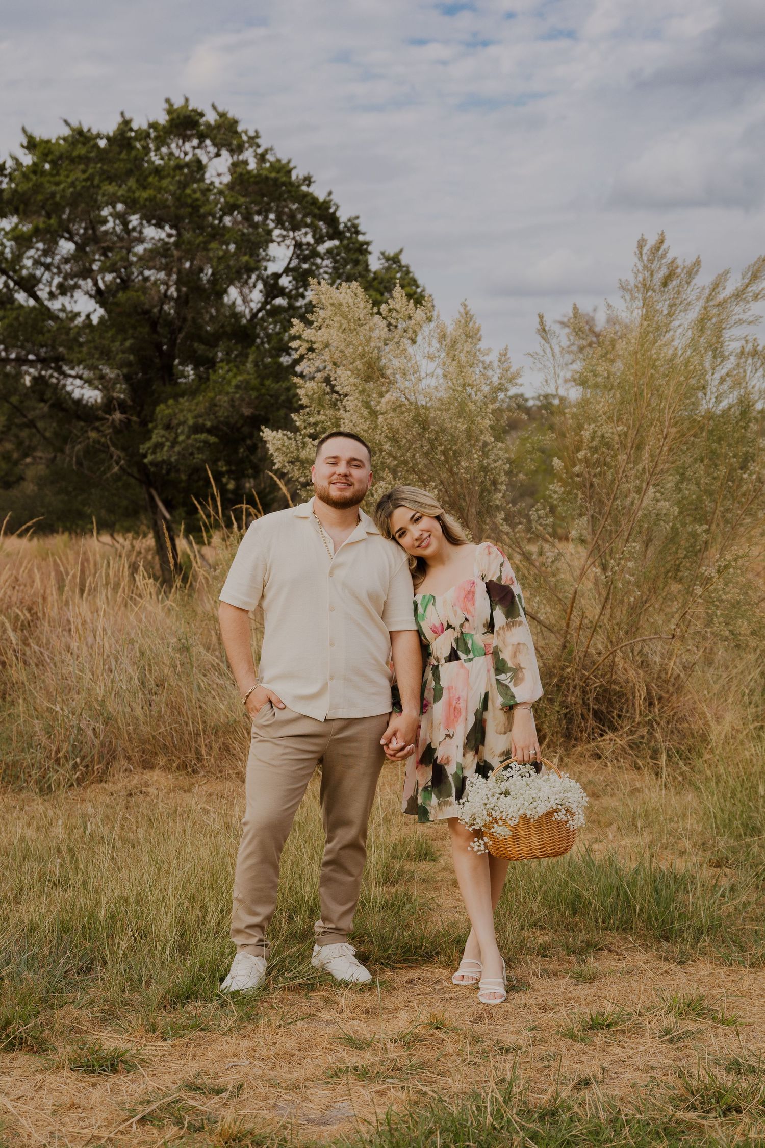 Couple in casual attire posing together in field during sunset for pregnancy announcement.