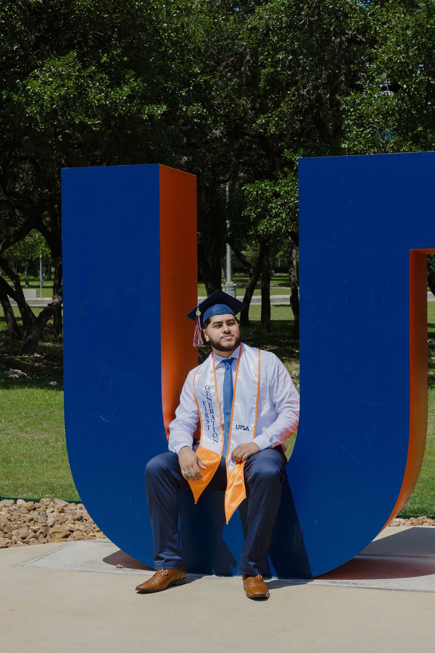 A large blue and orange letter U sculpture sits on a concrete path surrounded by green trees in a park setting.