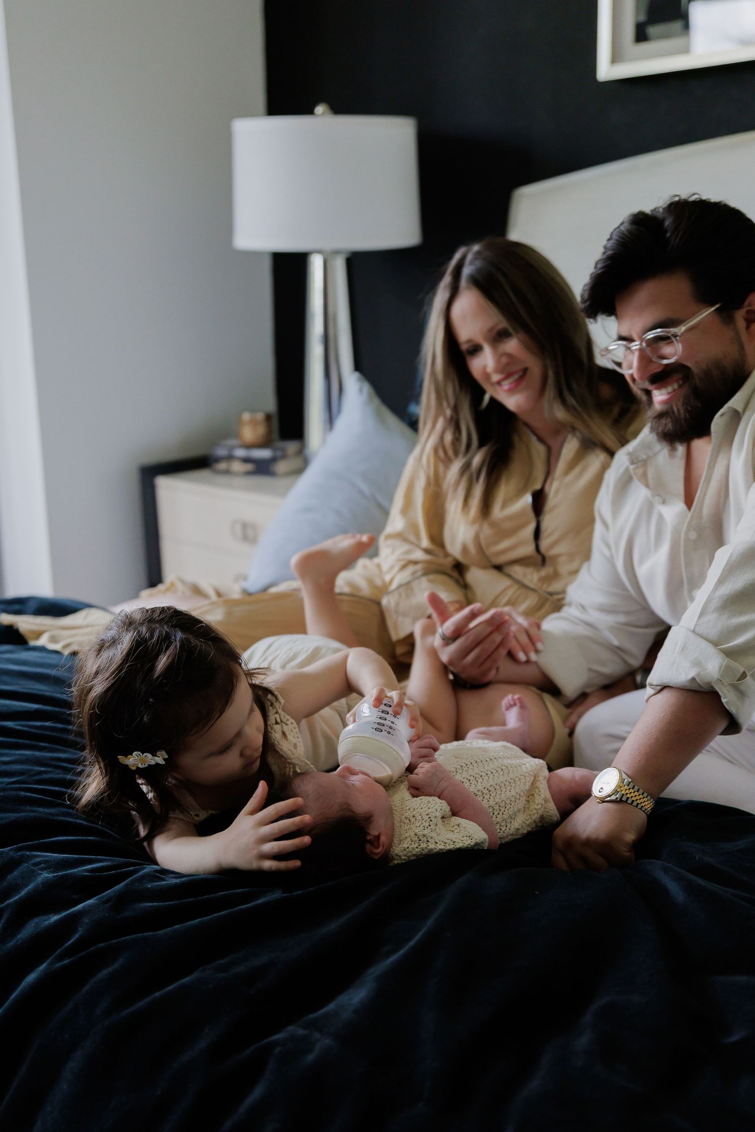 A series of intimate family moments captured in a bedroom showing parents bonding with their newborn baby on a dark bedspread.