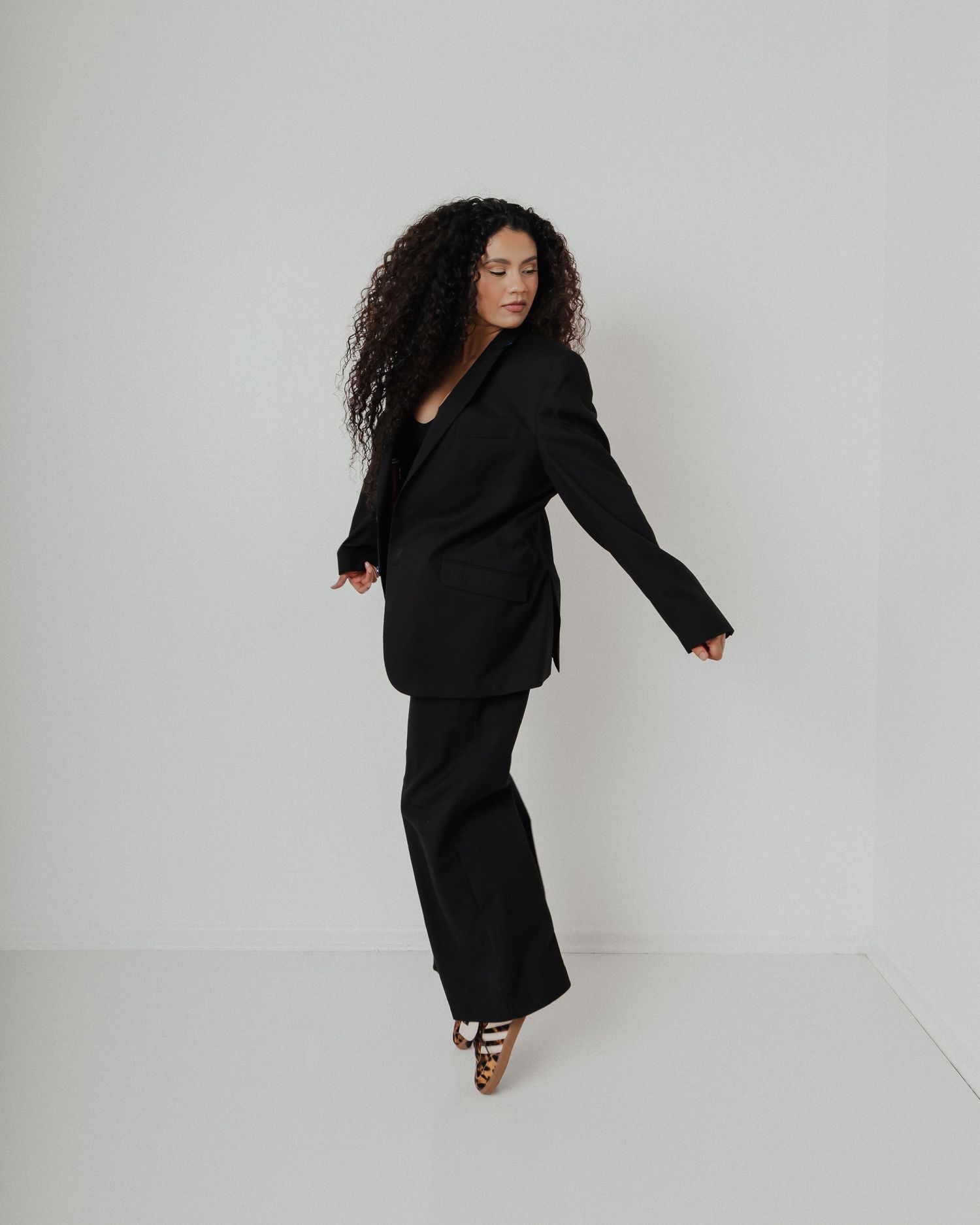 A model in a black power suit strikes a dynamic pose against a white studio background.
