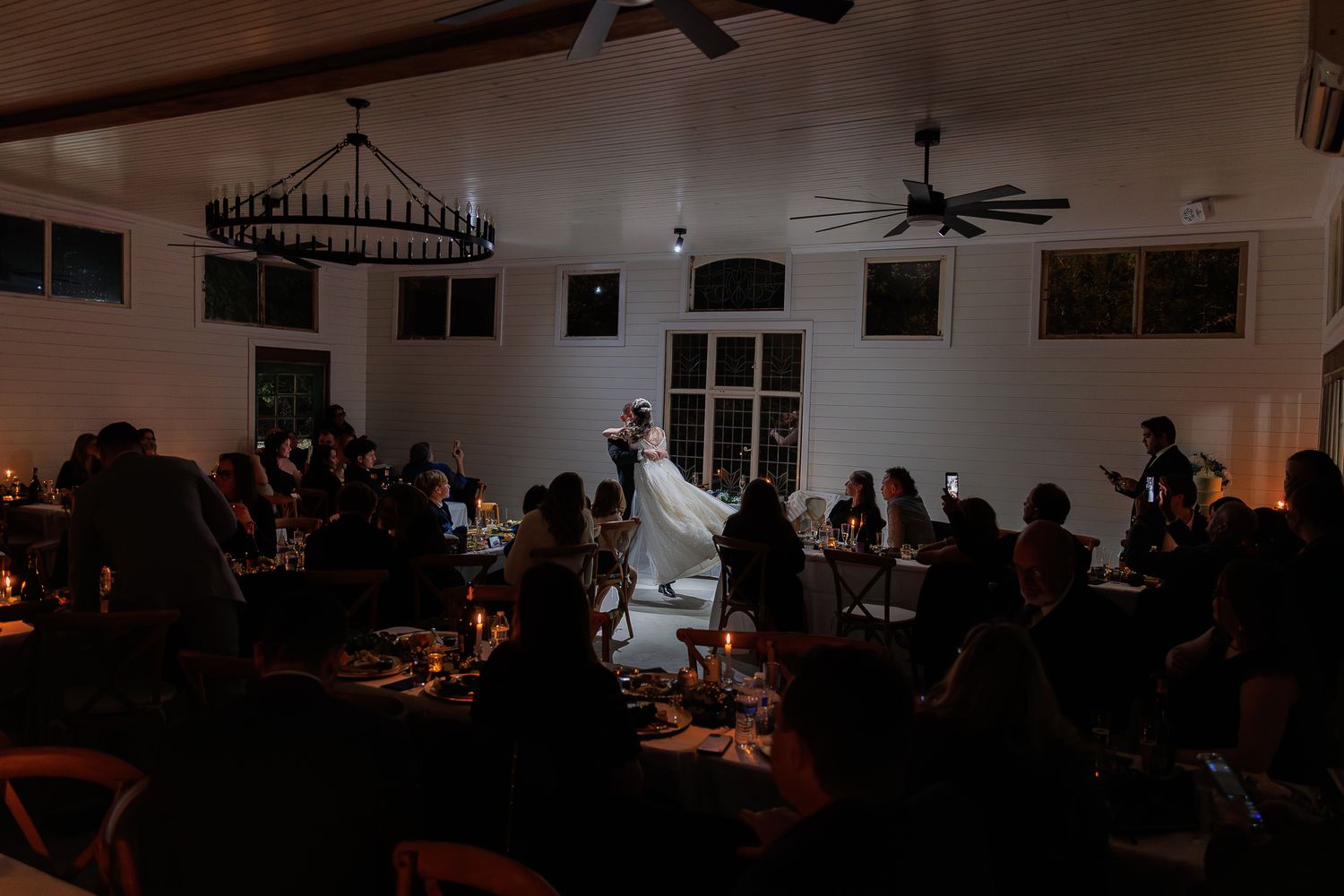 Dark silhouettes of wedding guests seated in a dimly lit reception venue with string lights overhead.