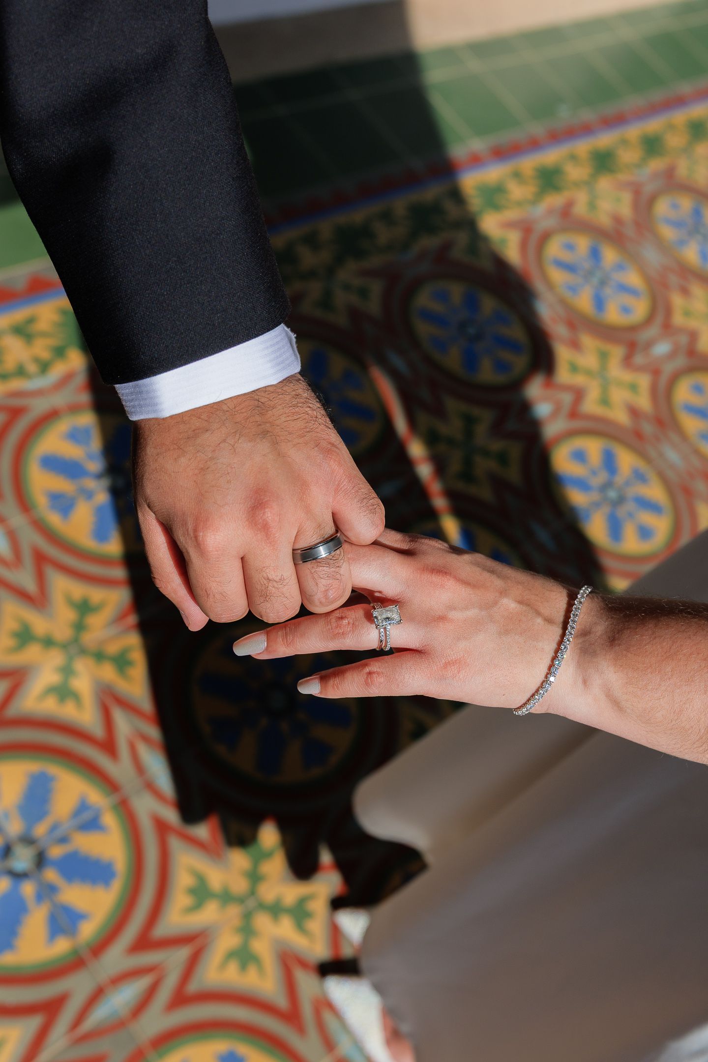 Close-up shots of hands exchanging rings during a wedding ceremony on a colorful mosaic floor.