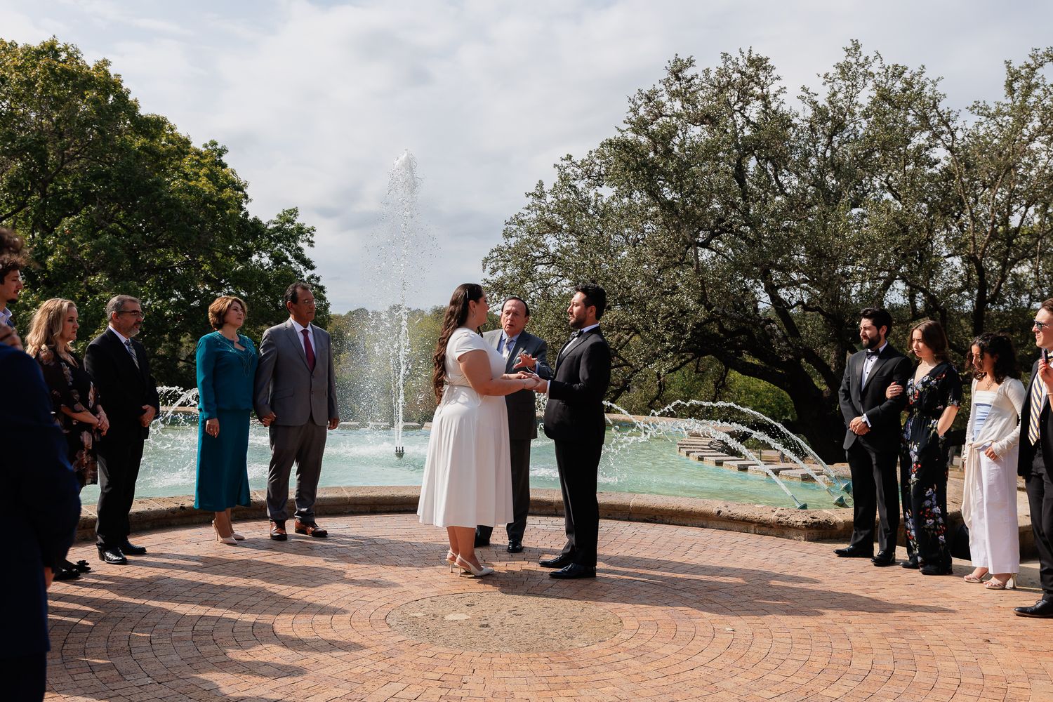 A group gathers at a scenic outdoor ceremony location overlooking a waterfront on a cloudy day.