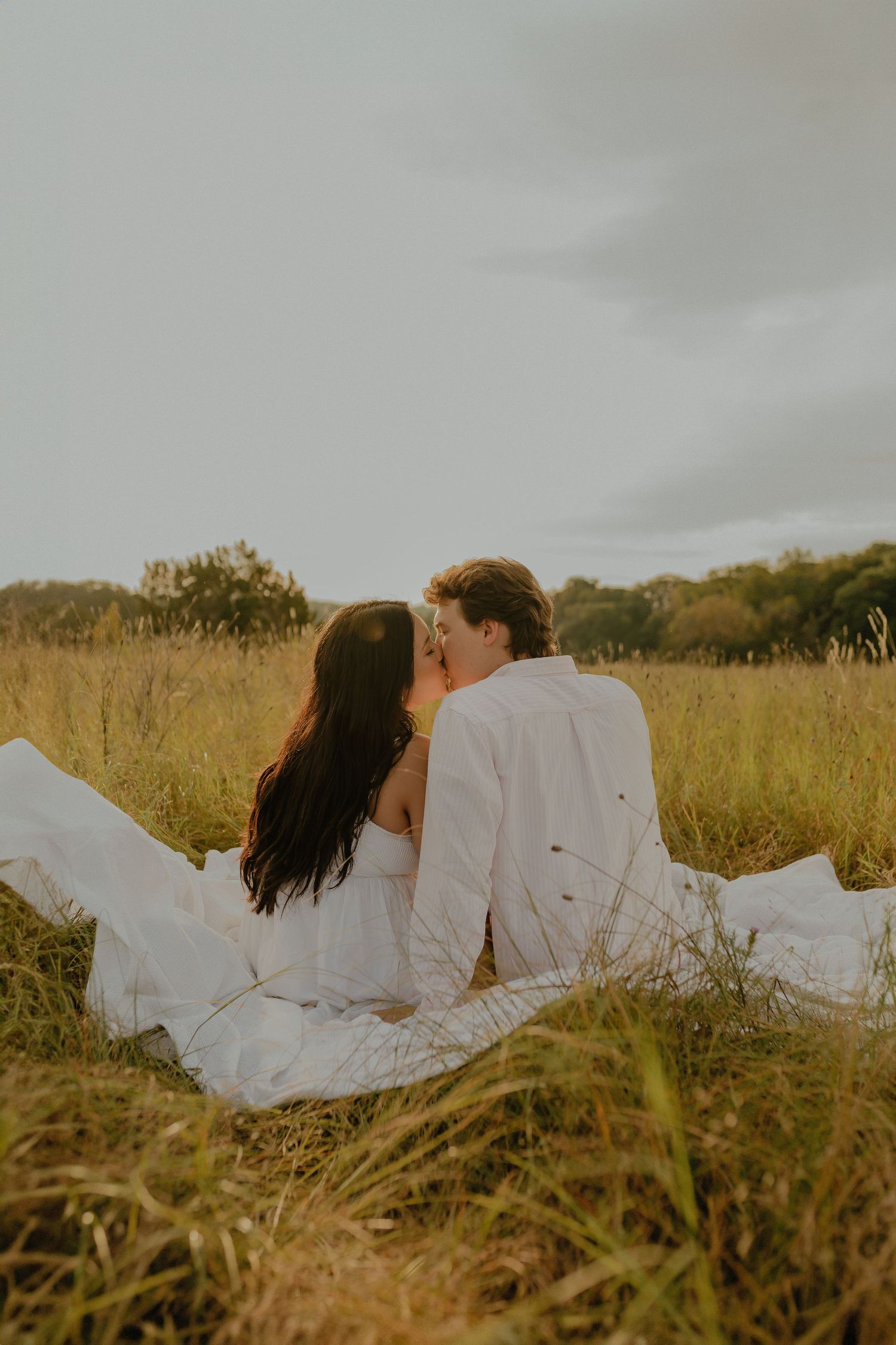 Couple in white clothing sitting close together in a meadow of tall grass.