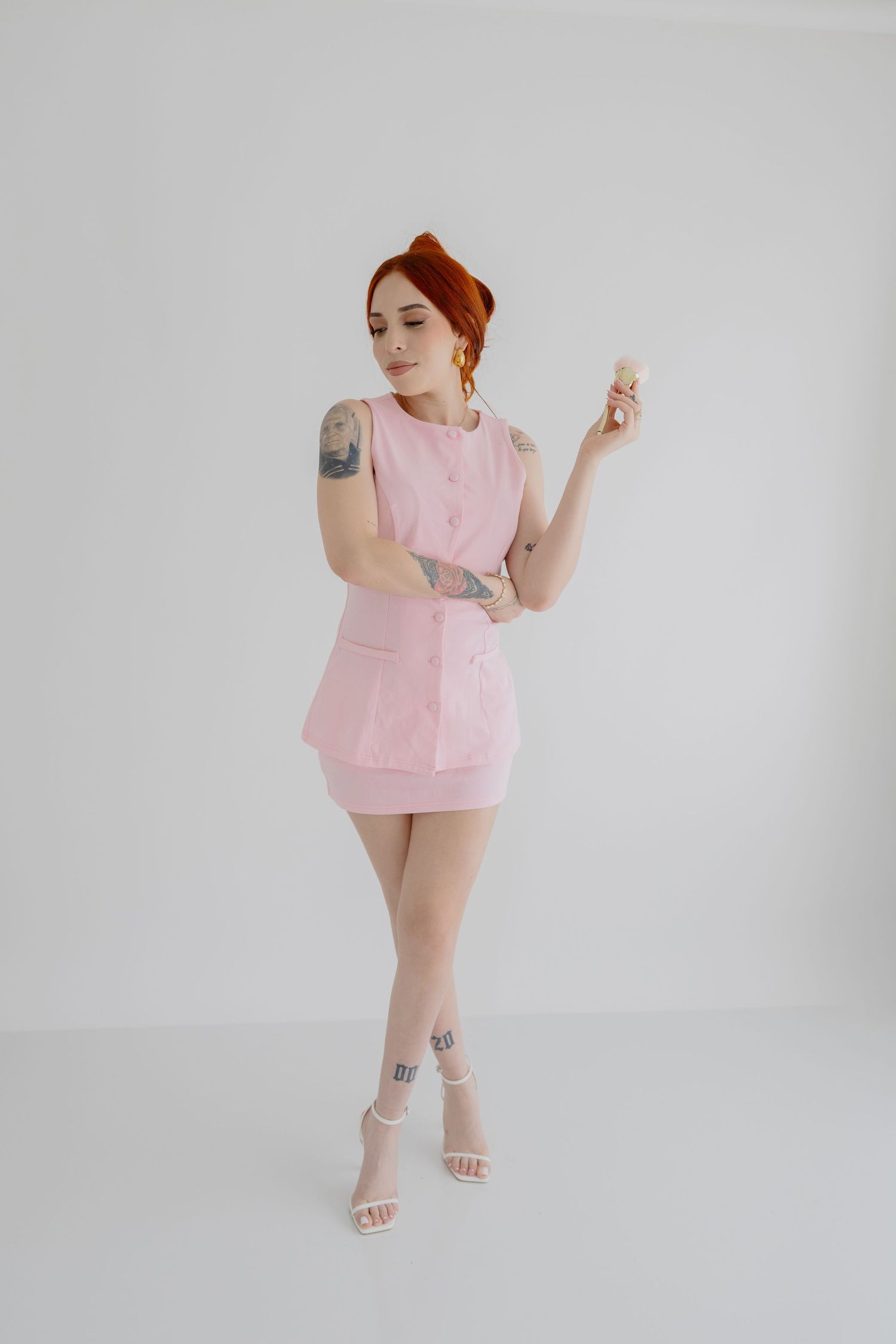 Woman in pink mini dress strikes pose against white backdrop.