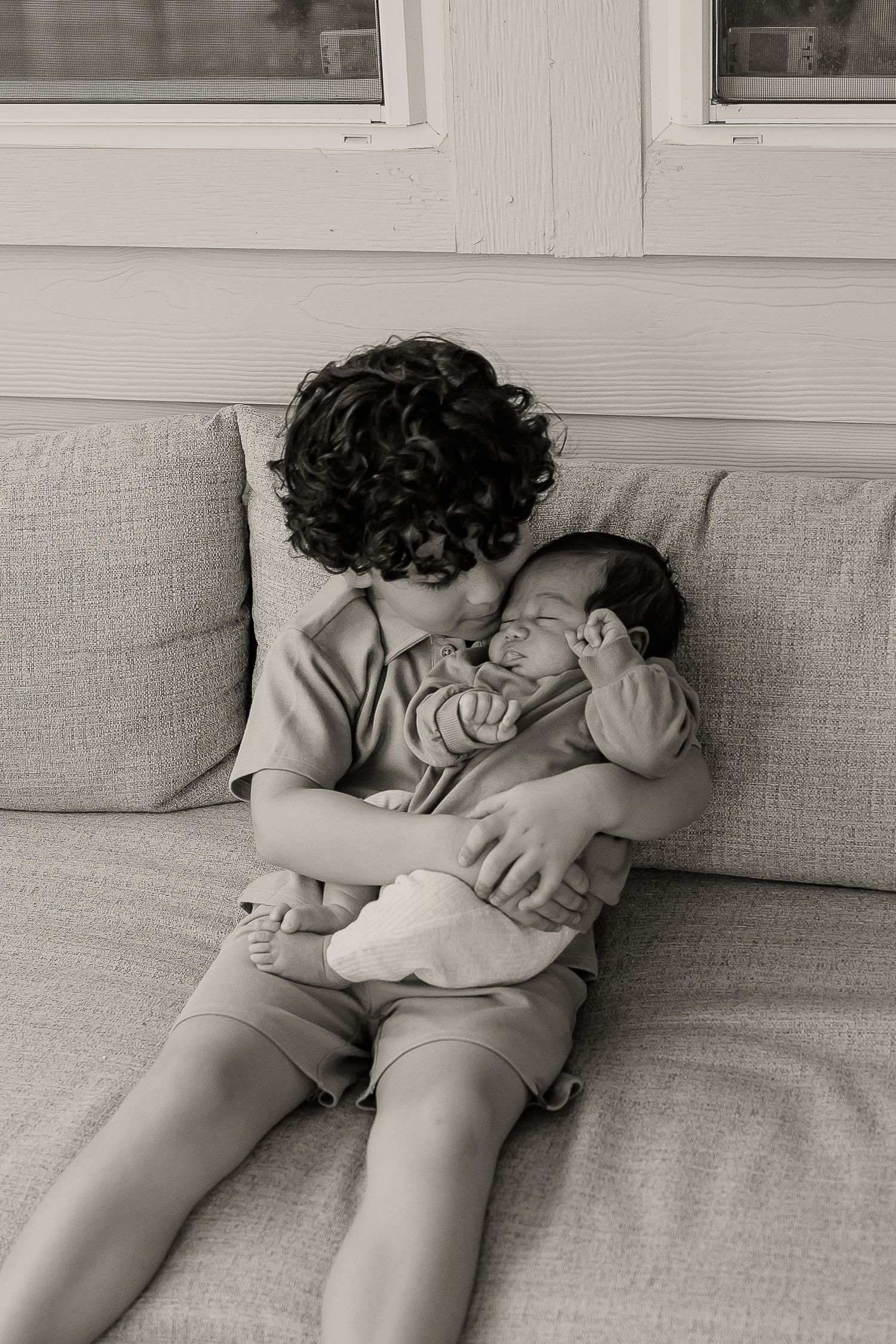 A tender black and white moment captured on a couch as siblings share a loving embrace.