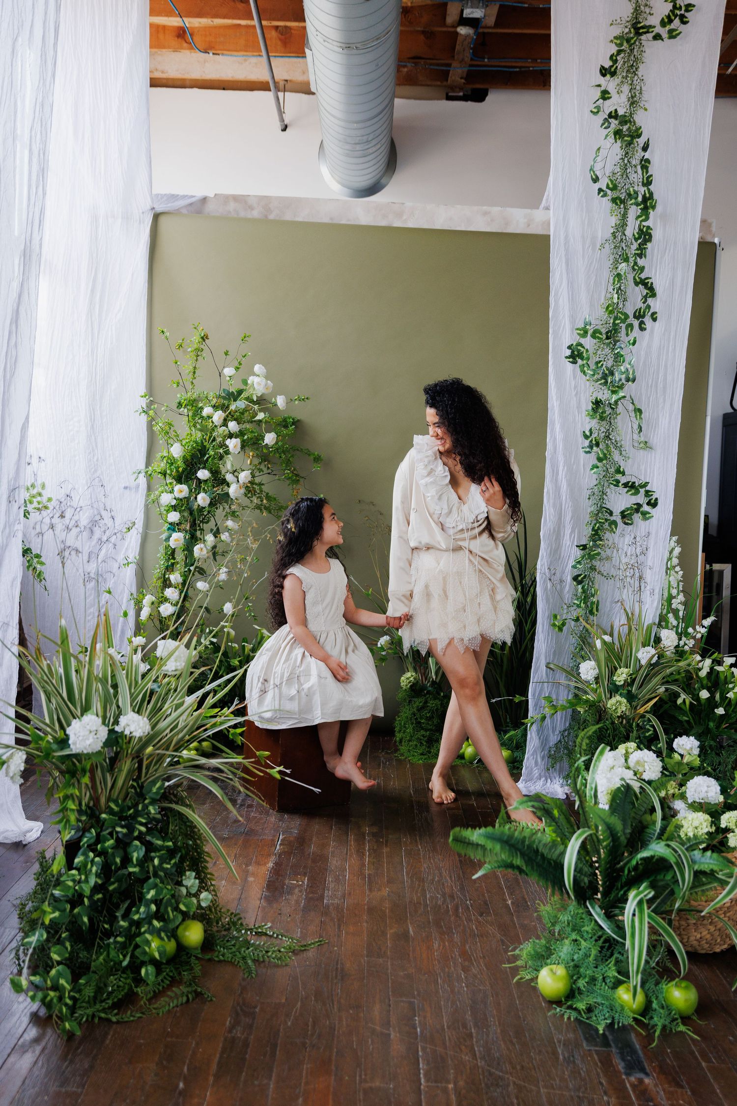 Artistic bridal portraits in a loft space with white curtains, greenery and floral decorations creating an ethereal atmosphere.