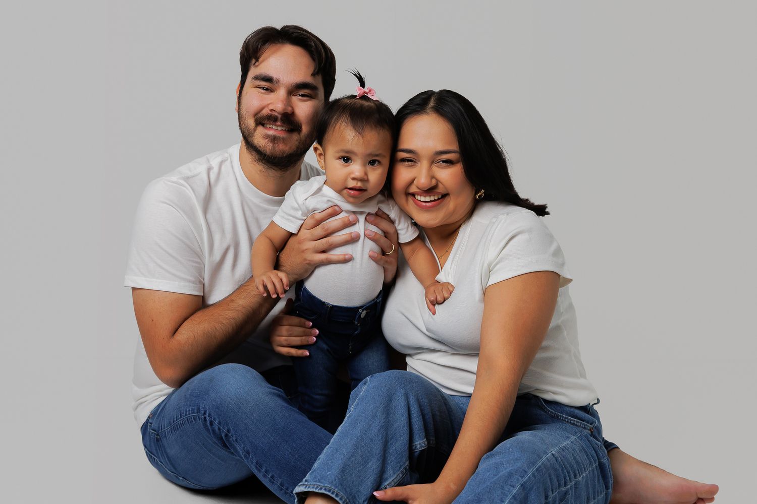 A family wearing white shirts and blue jeans poses together against a white background in a series of photos.