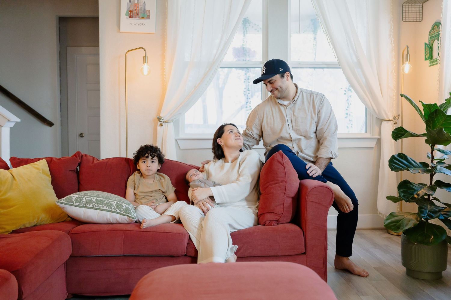 A family relaxing together on a red couch in a bright living room.
