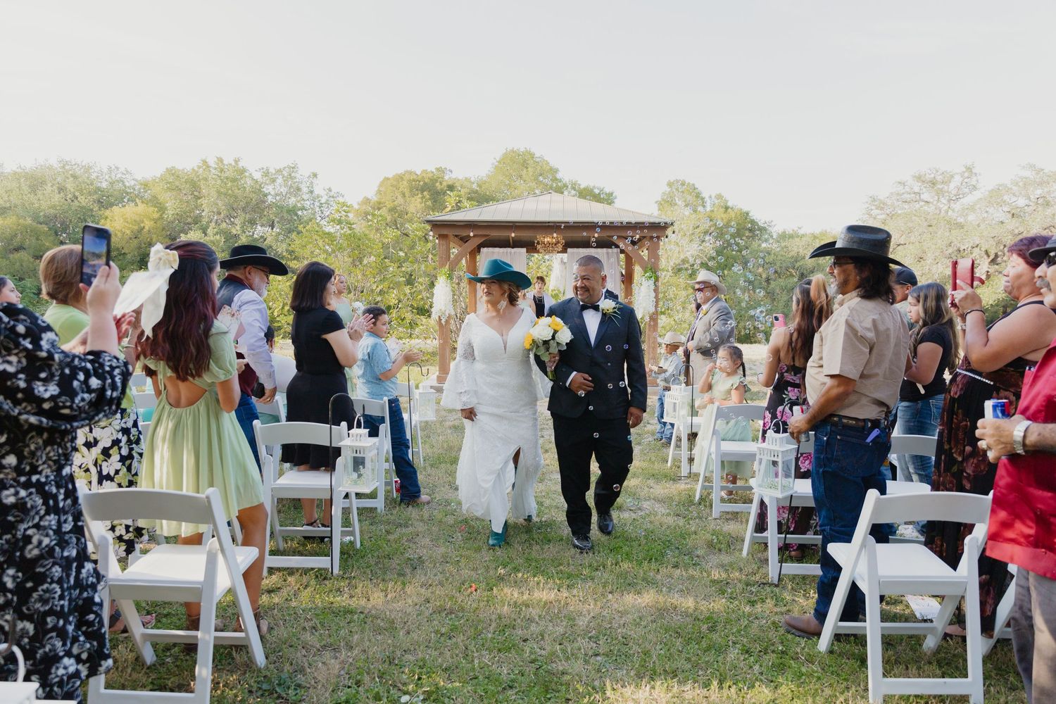 Wedding recessional with couple walking down aisle between rows of white chairs outdoors.