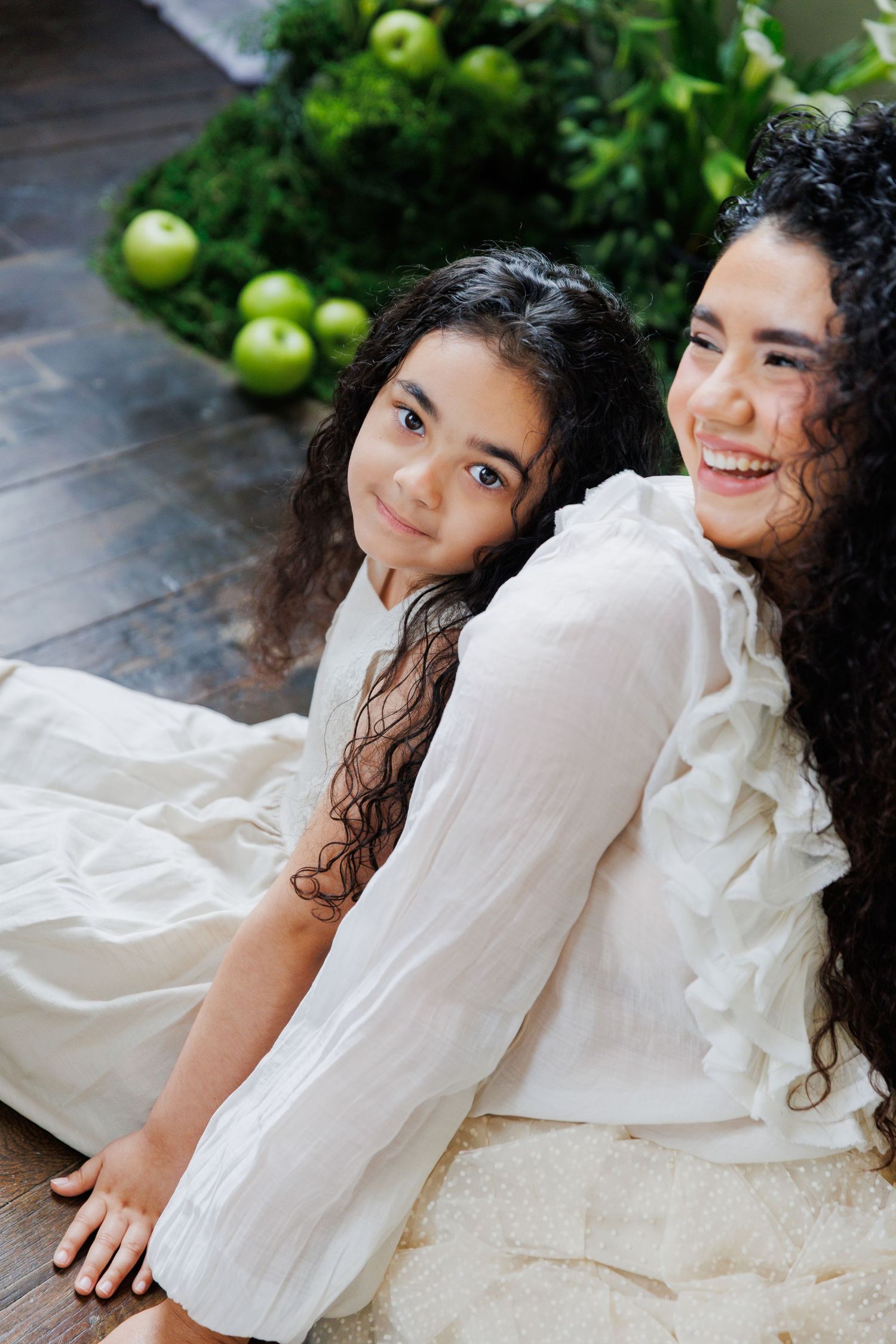 A series of artistic portraits in a garden setting with green apples and white ruffled clothing against a dark background.
