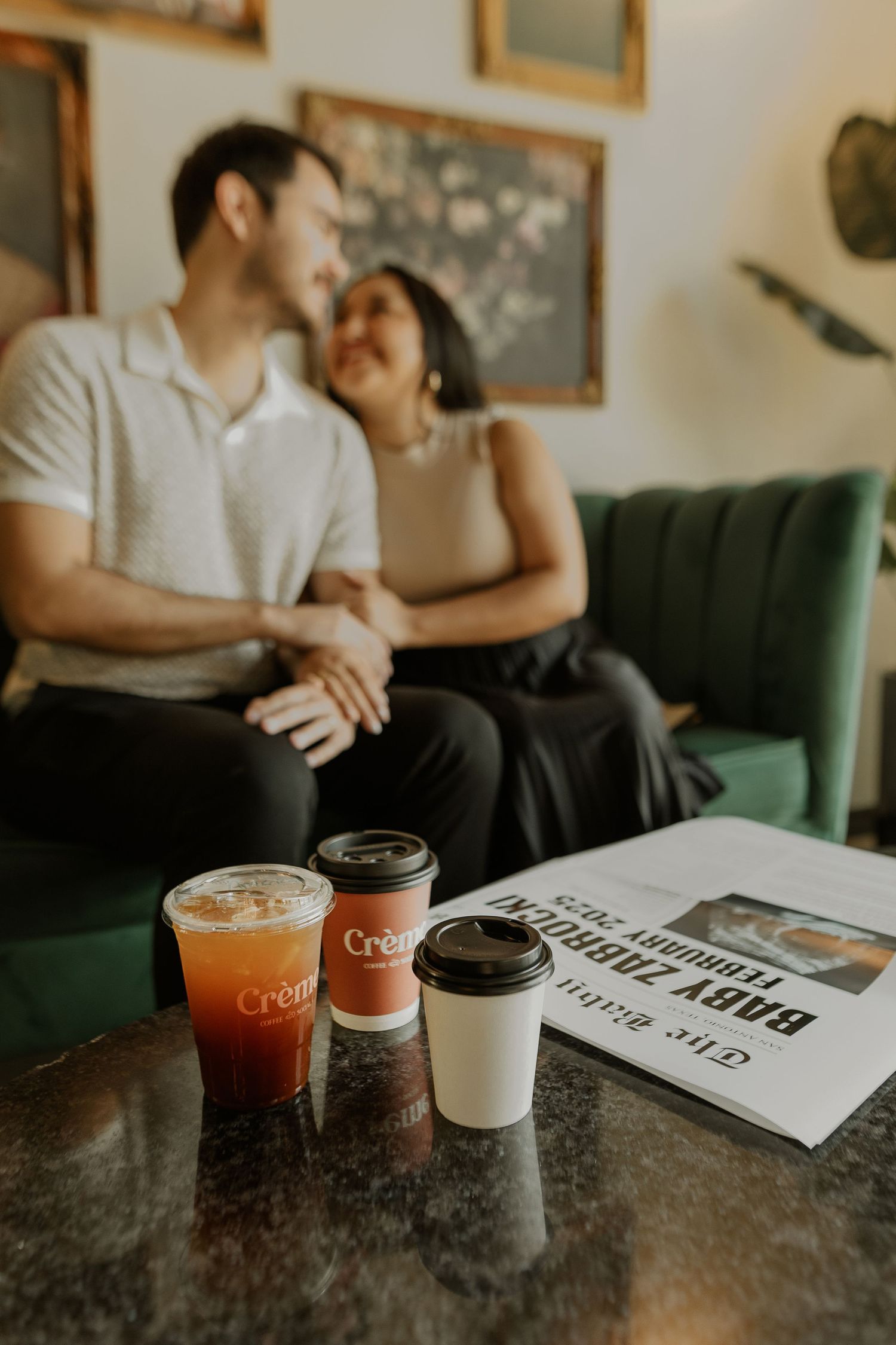 Cozy cafe scene with drinks and newspaper on table near green velvet couch.