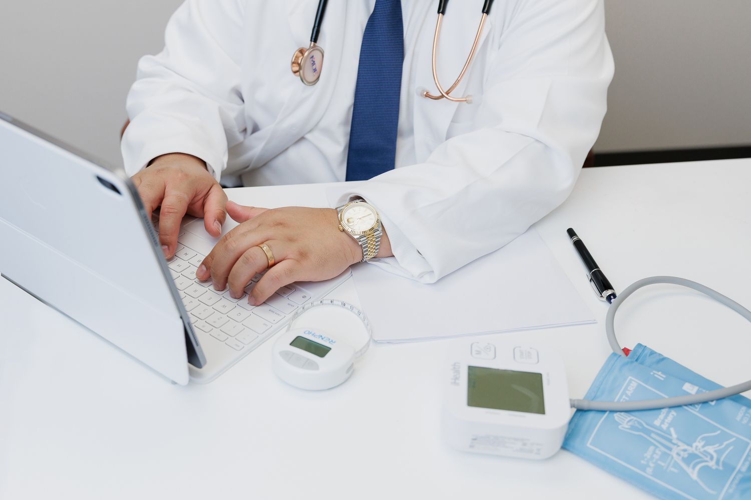 Medical professional in white coat reviews patient records while sitting at office desk with stethoscope.