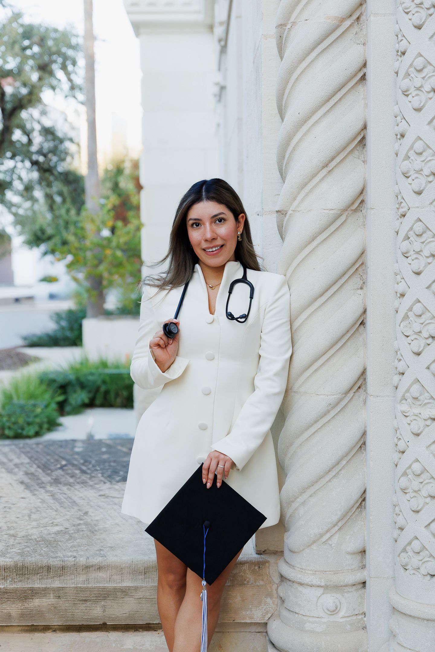 Professional wearing a white blazer and stethoscope poses confidently against an ornate architectural column.