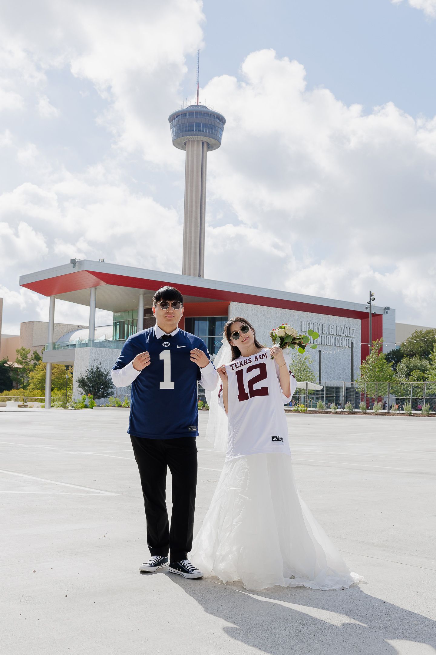 Wedding couple wearing sports jerseys pose together with Tower of Americas visible in San Antonio skyline.