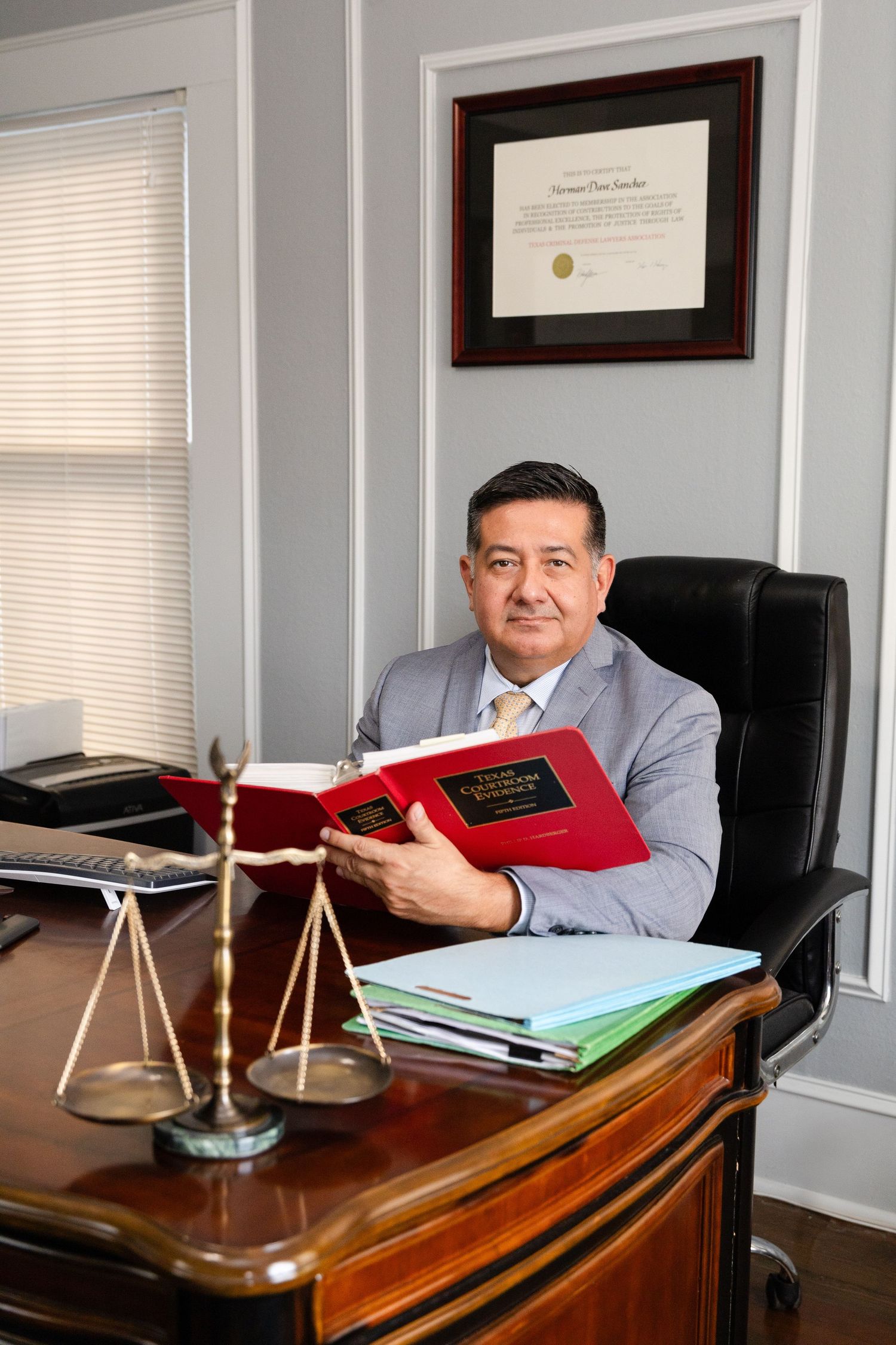Professional in grey suit sitting at desk with law books and scales of justice decor.