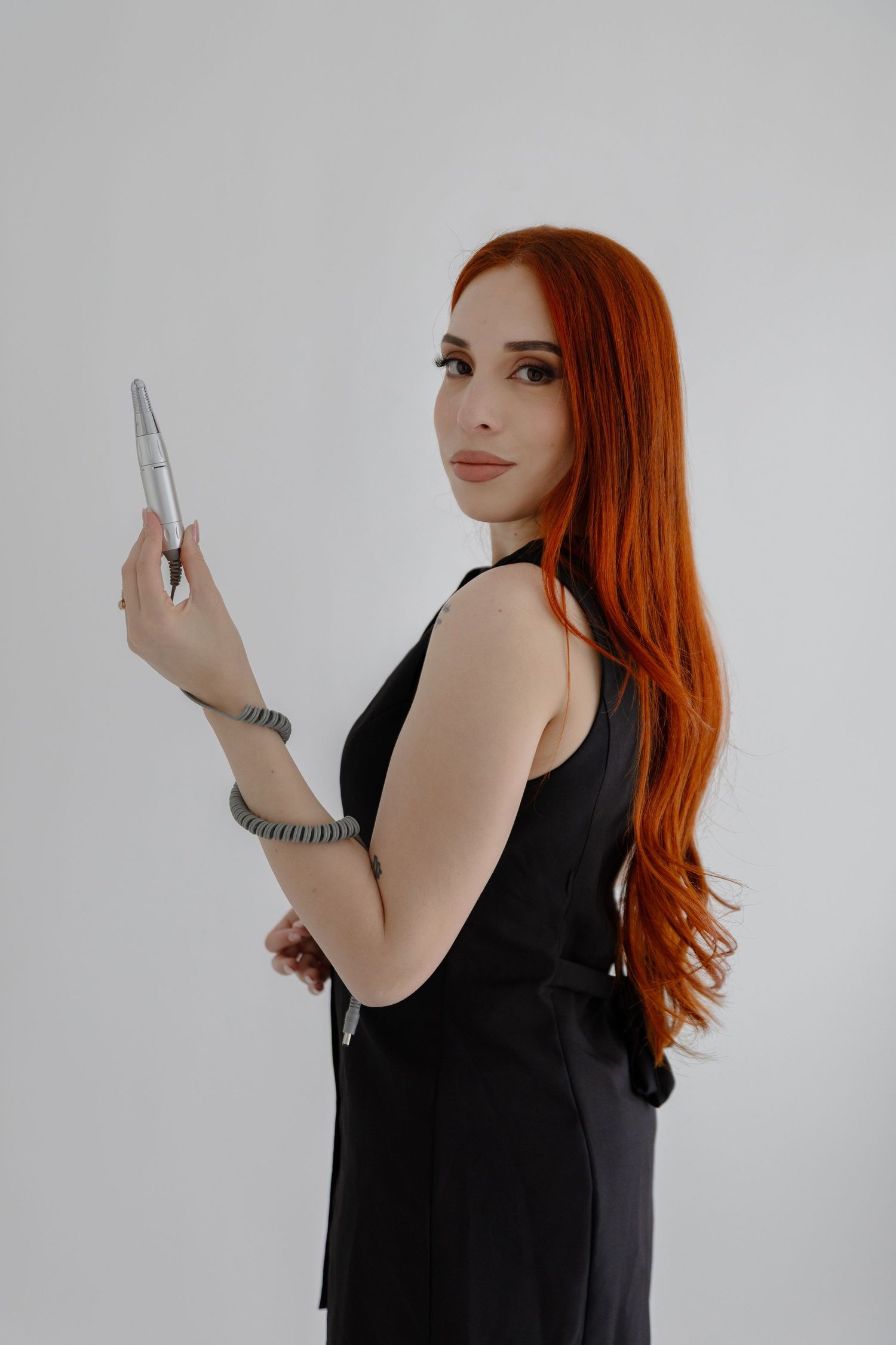 Woman with vibrant red hair holds pen while posing in black outfit.