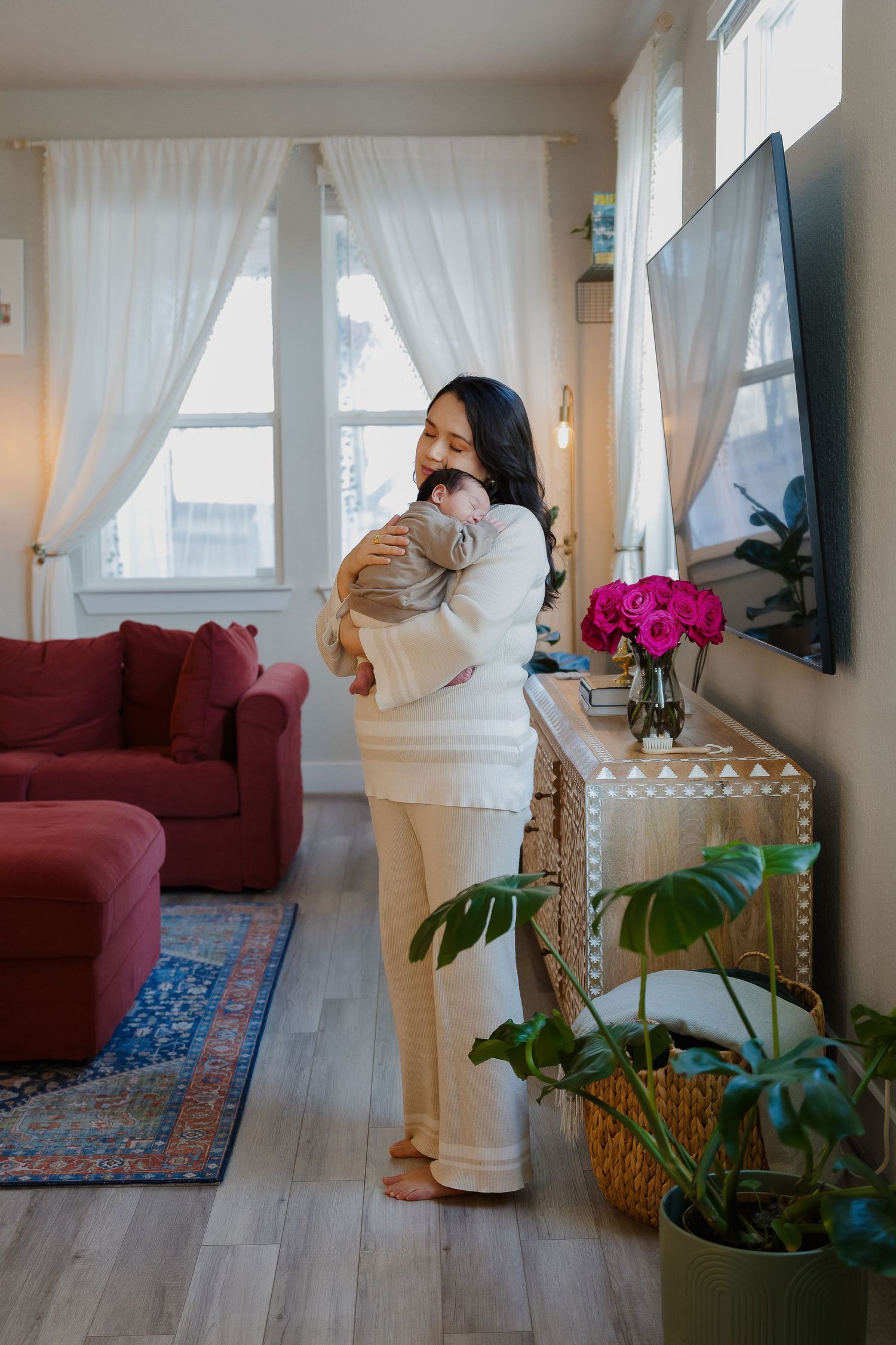 Person in white holding a cat in a modern living room with red furniture and plants.