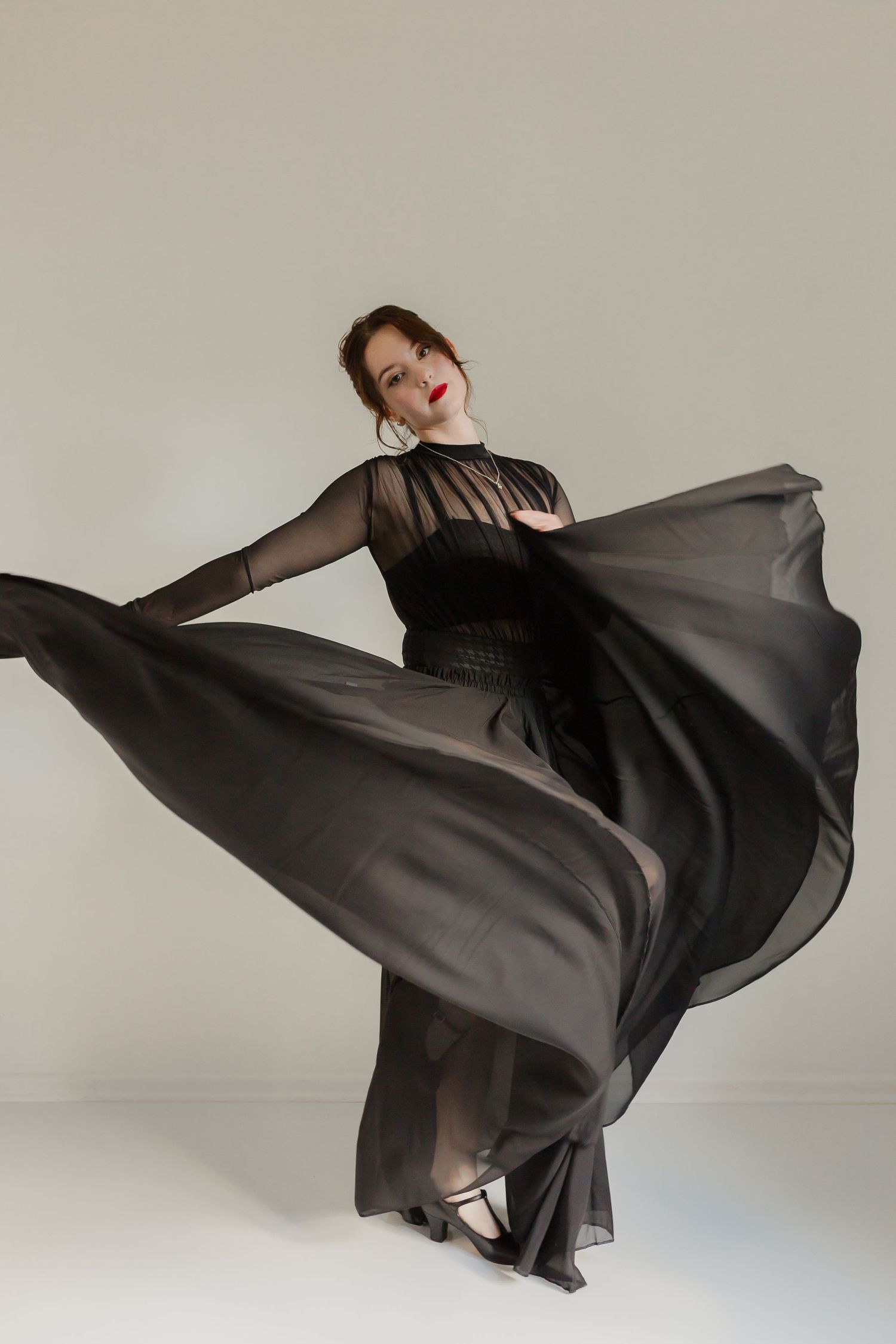 Dancer in flowing black sheer dress twirling dramatically against light background.