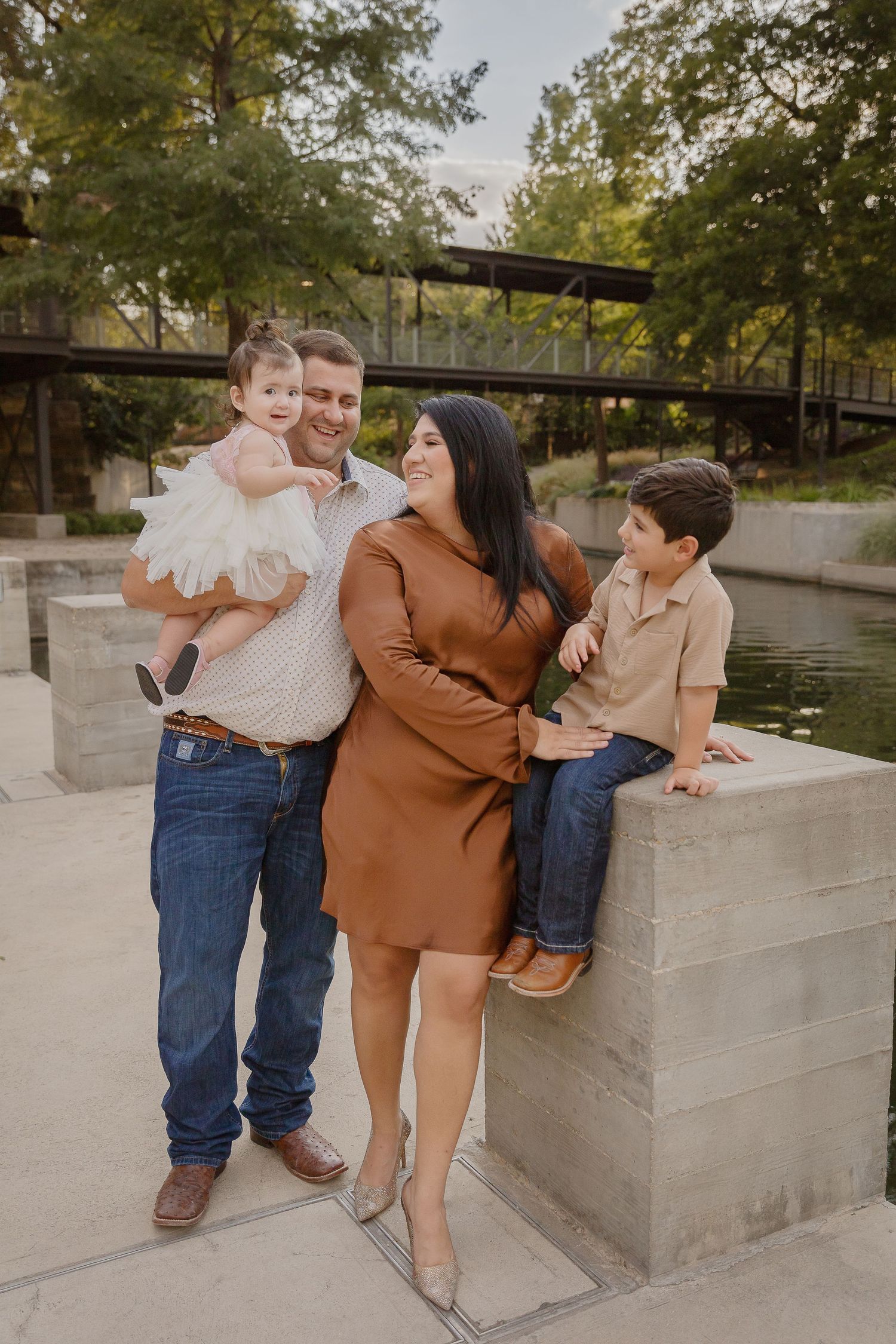 A family poses together outdoors near a pond and bridge on a sunny autumn day.