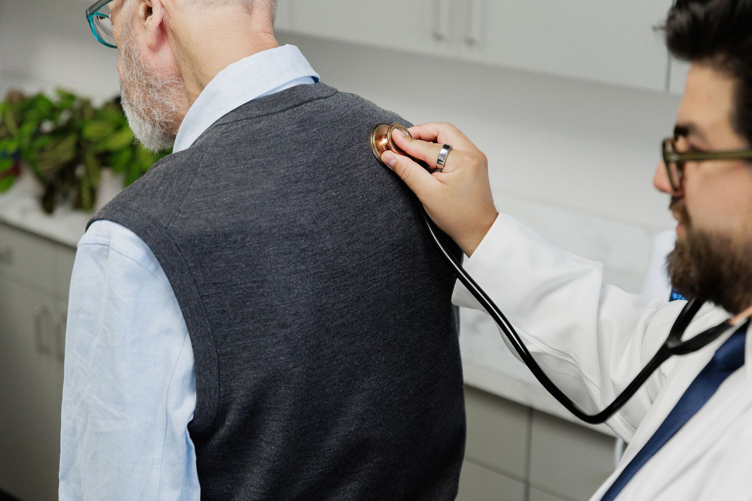 Medical professional using stethoscope to examine patient's back during physical checkup.