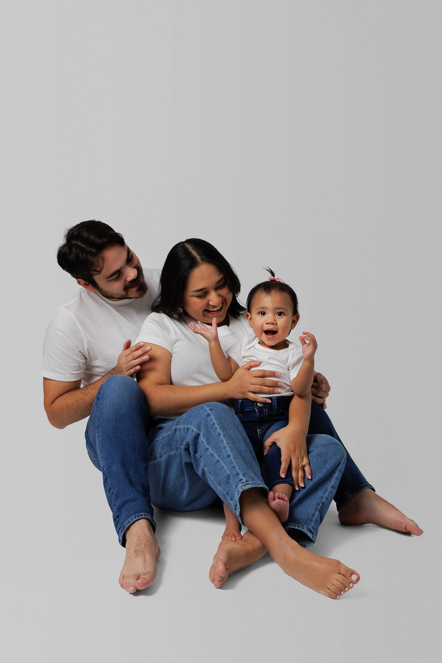 Family in casual white shirts and jeans sit together on white background showing progression of loving poses.