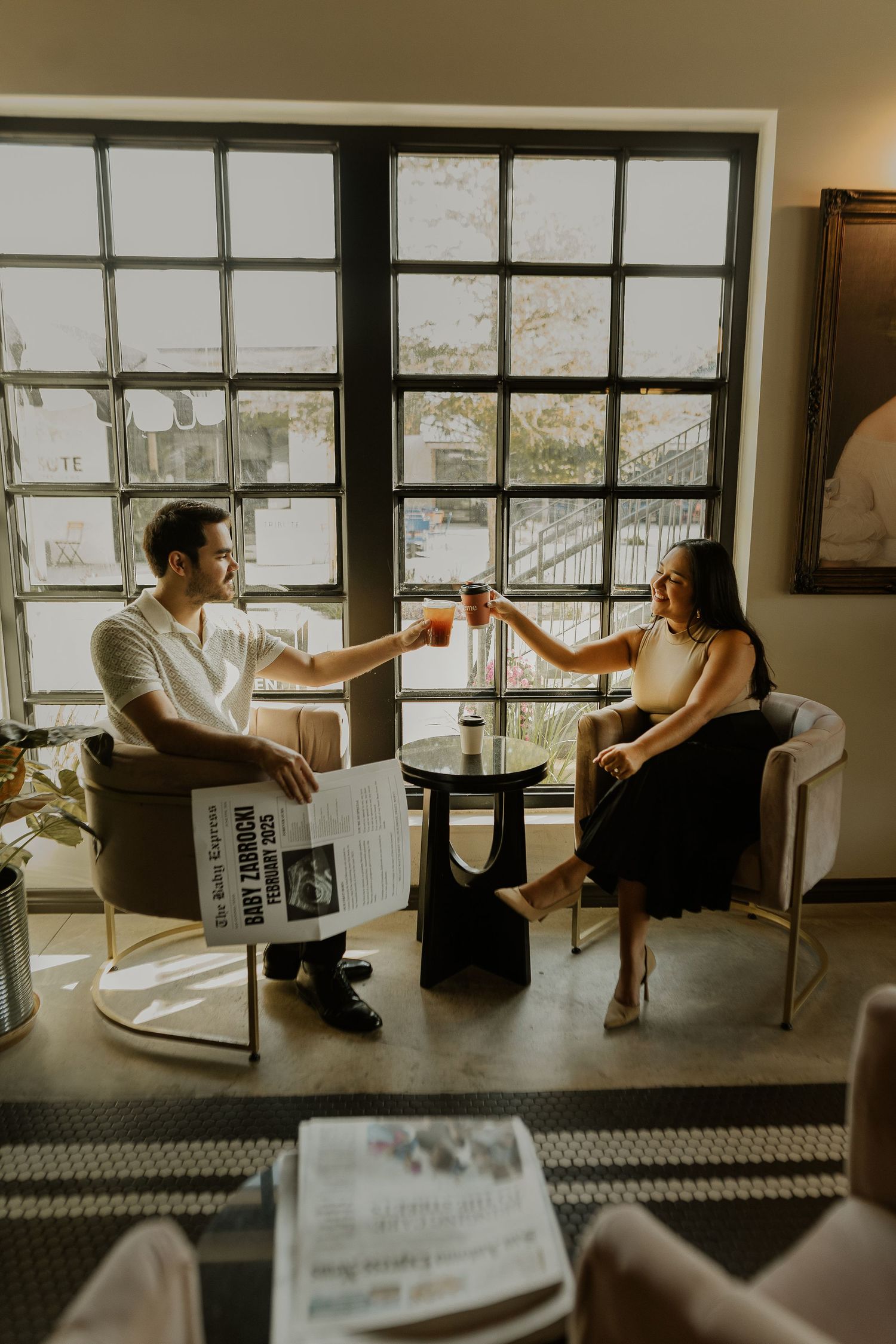 Two people share drinks by a large window in a bright cafe setting.