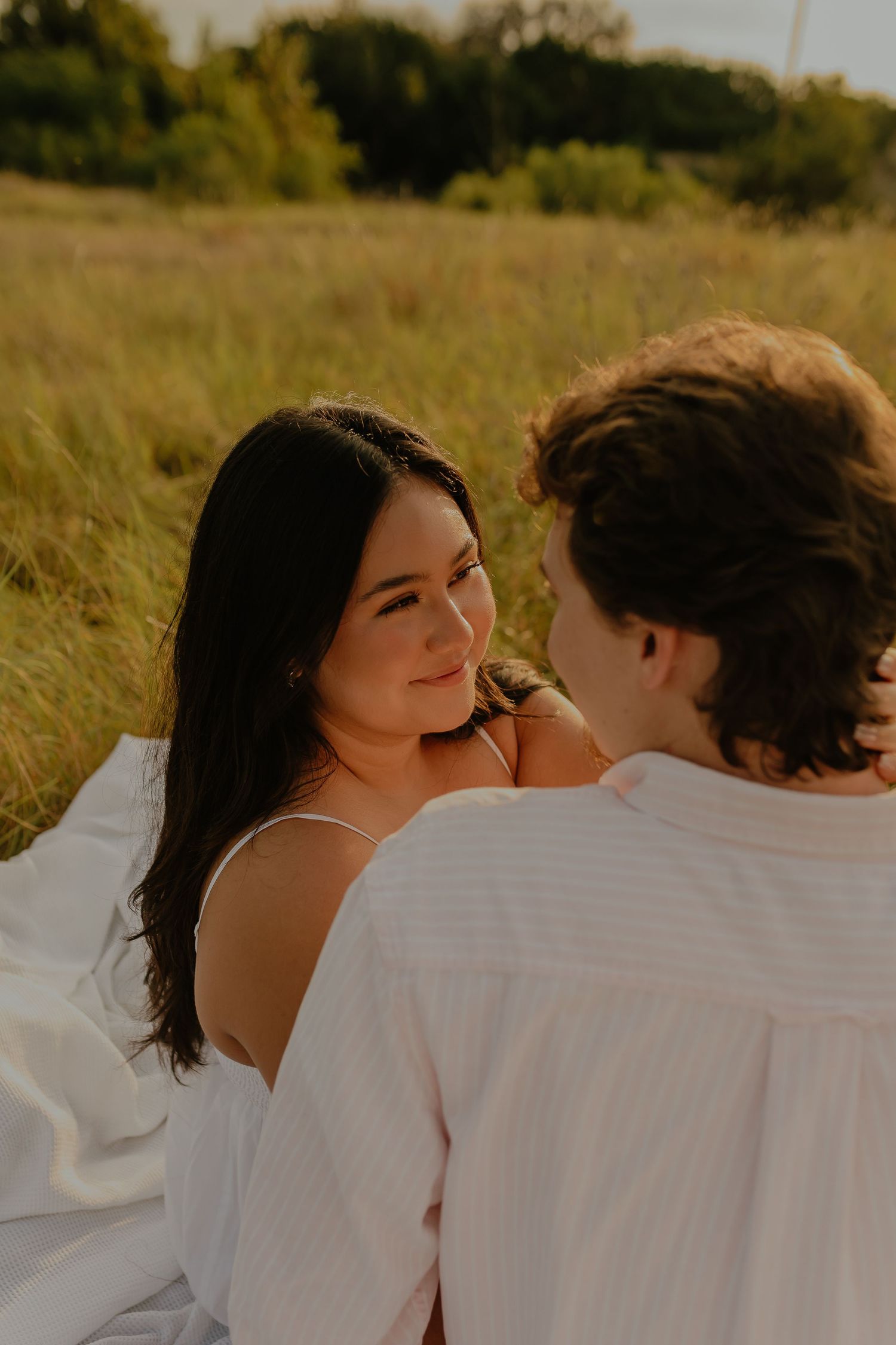 Couple sharing a tender moment on a white blanket in golden grass at sunset.