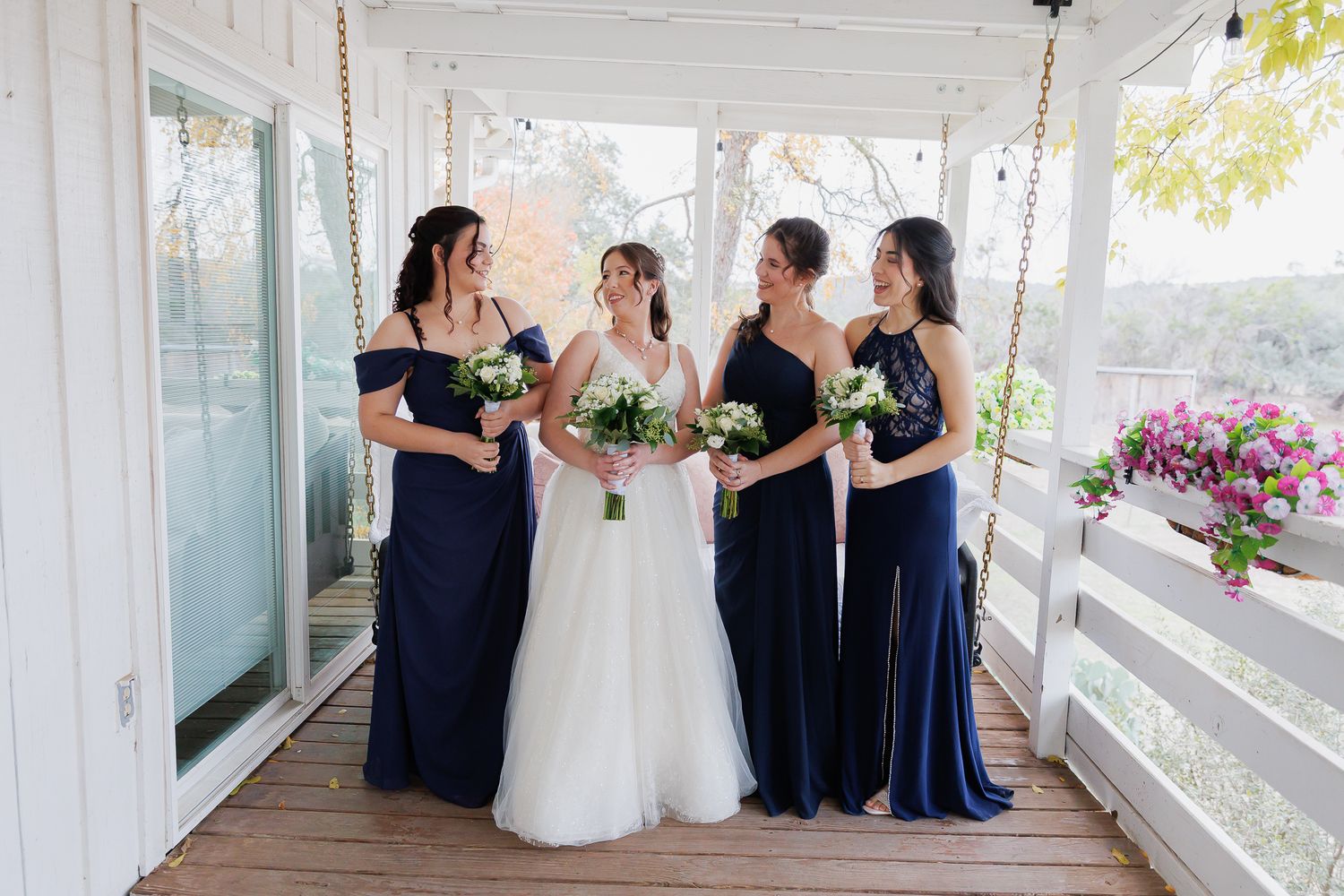 Wedding party members in navy blue and white attire gather on a bright sunlit porch for formal photos.