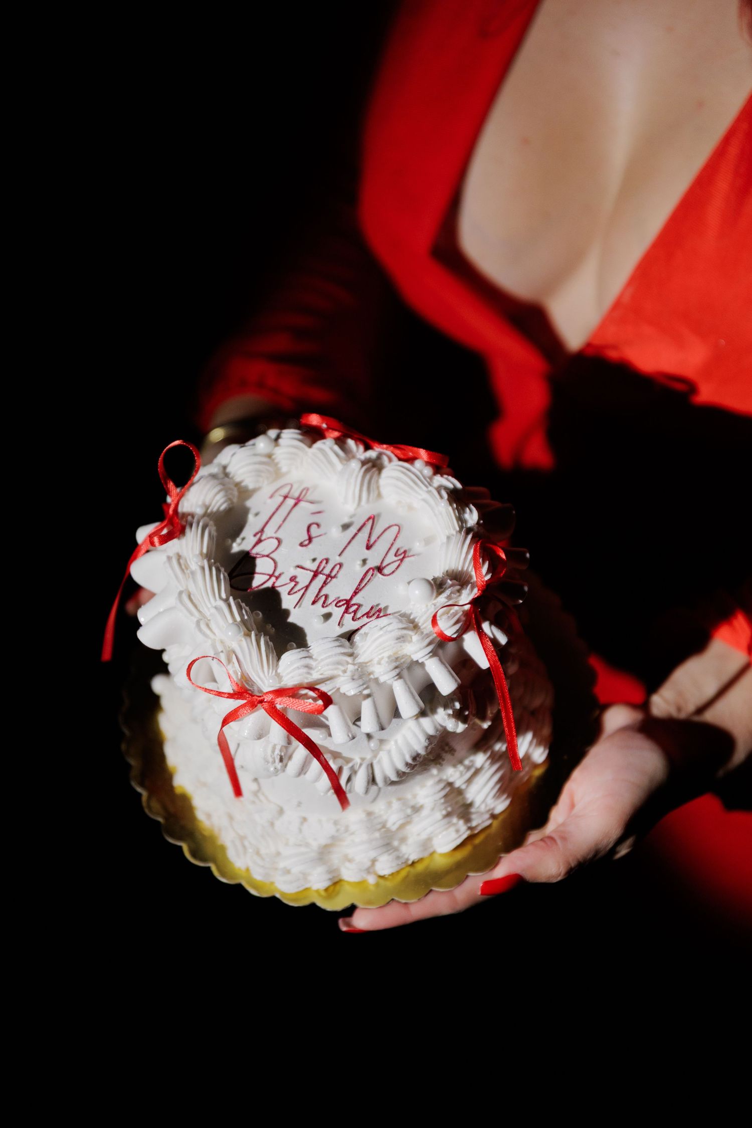A sequence showing a white frosted cake with red ribbons being presented against a dark background.