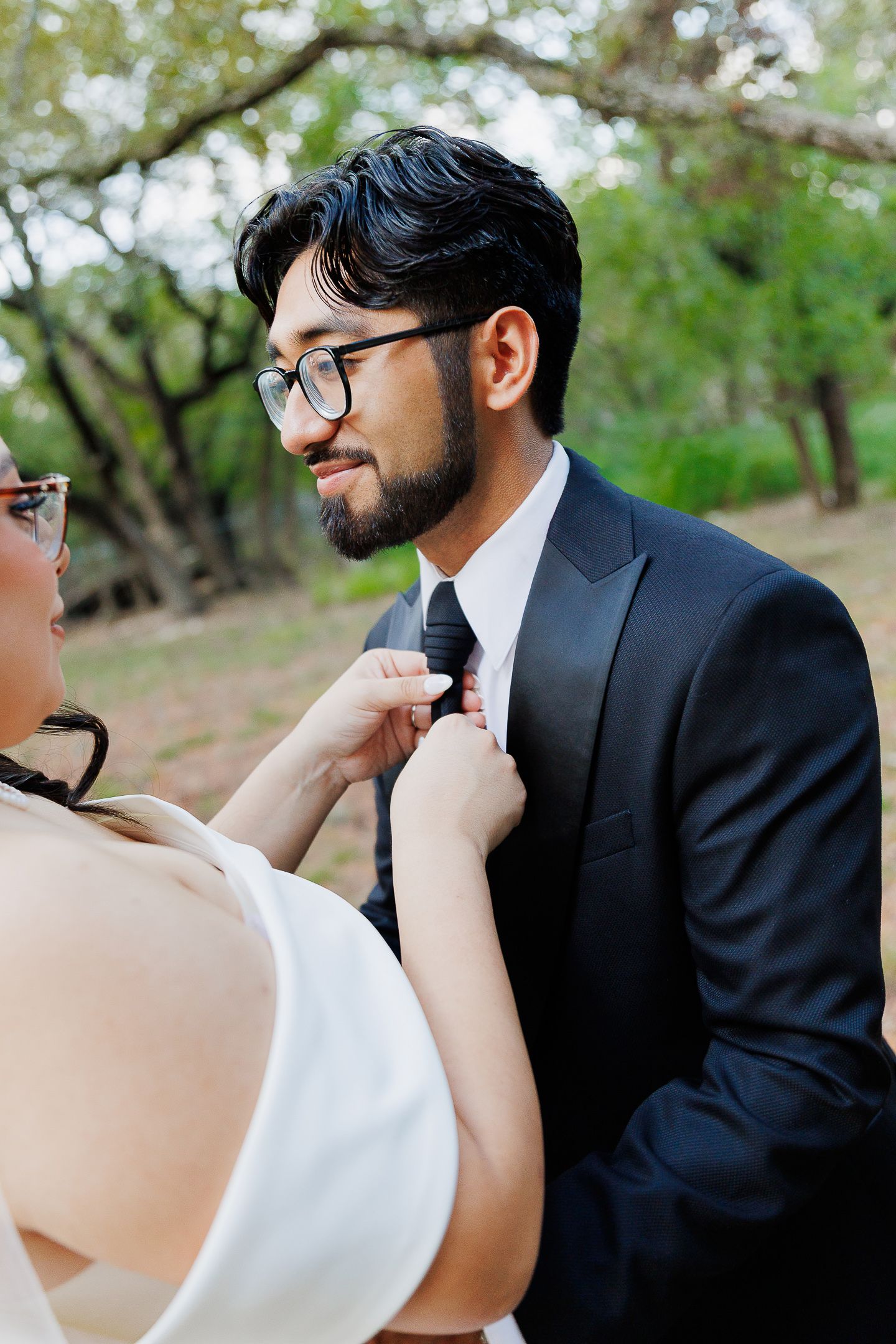 A couple in wedding attire share a romantic moment outdoors under blooming trees in spring.