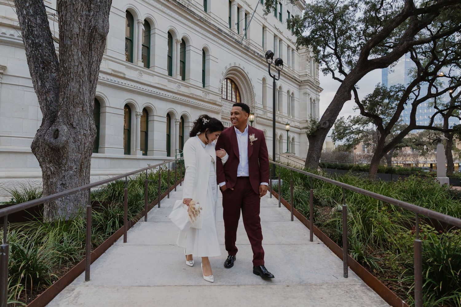 Couple poses on elegant white stone pathway surrounded by greenery.