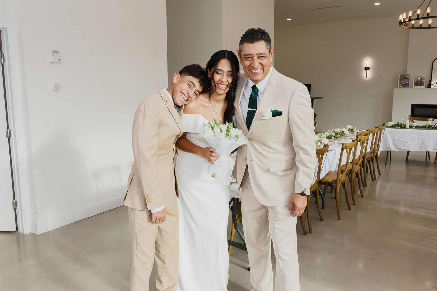 Three people in formal attire sharing a joyful moment in a modern white reception venue.