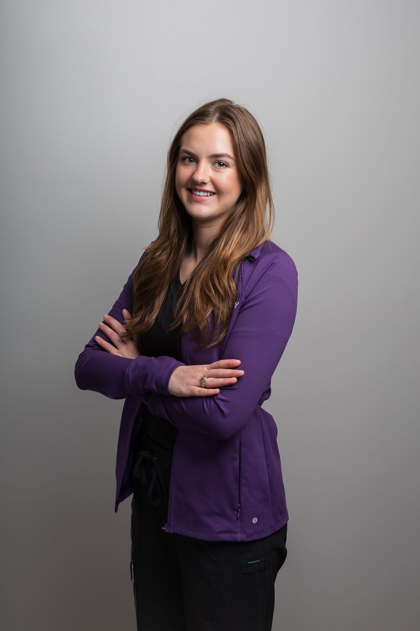 Professional portrait of someone in a purple cardigan posing with crossed arms against a gray background.