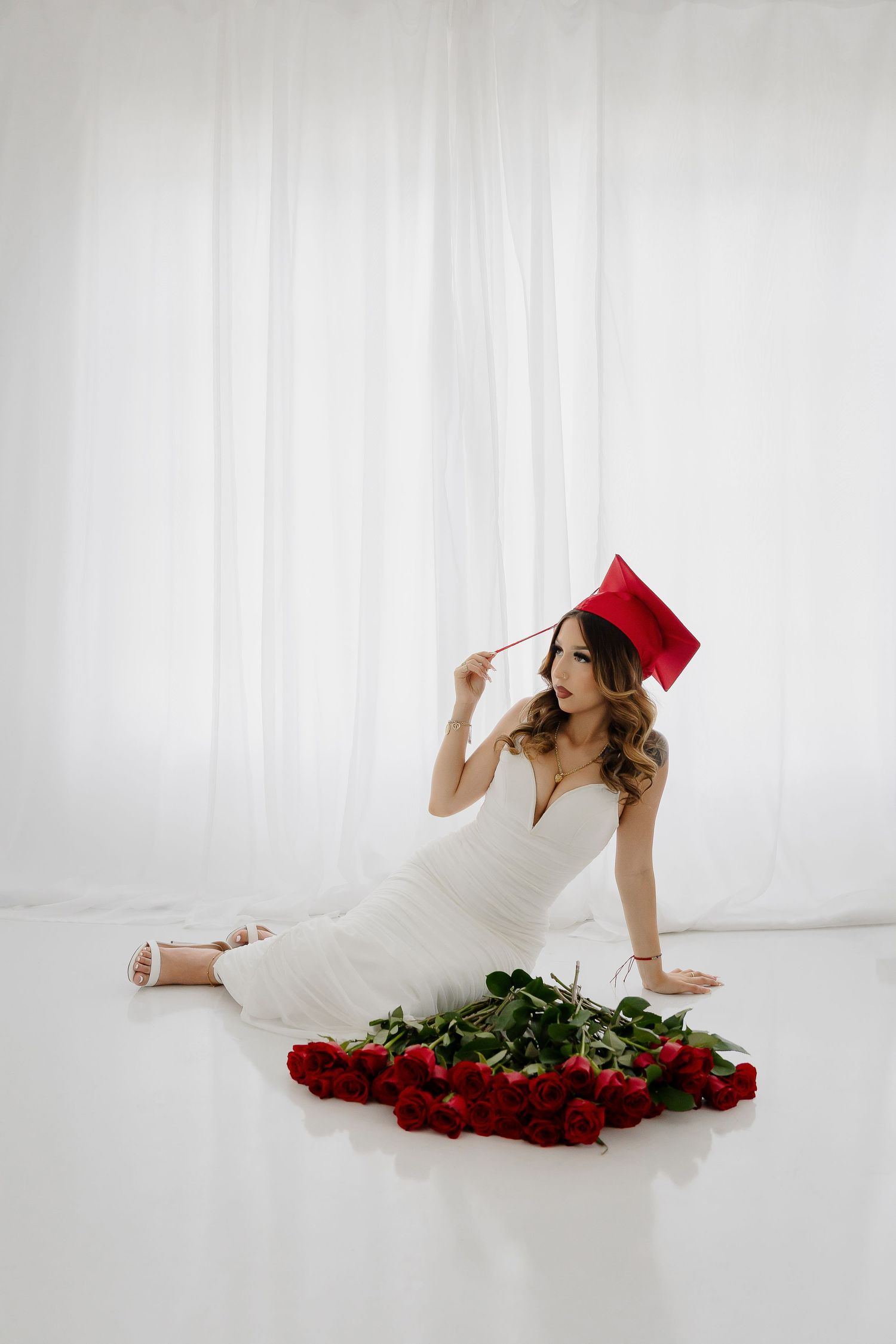 Graduation portrait with red cap and white dress surrounded by red roses.
