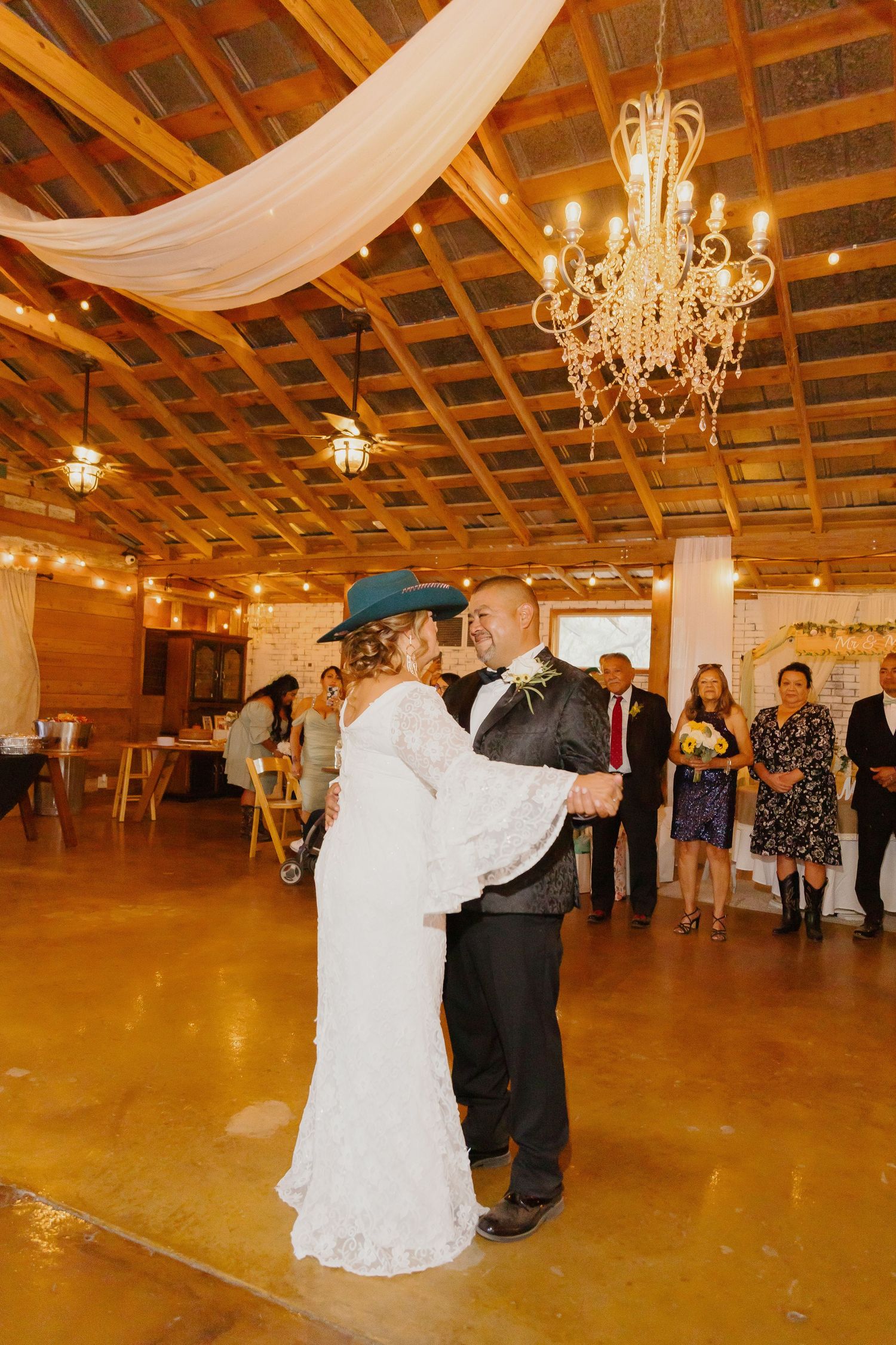 First dance in rustic venue with wooden beams and elegant chandelier overhead.
