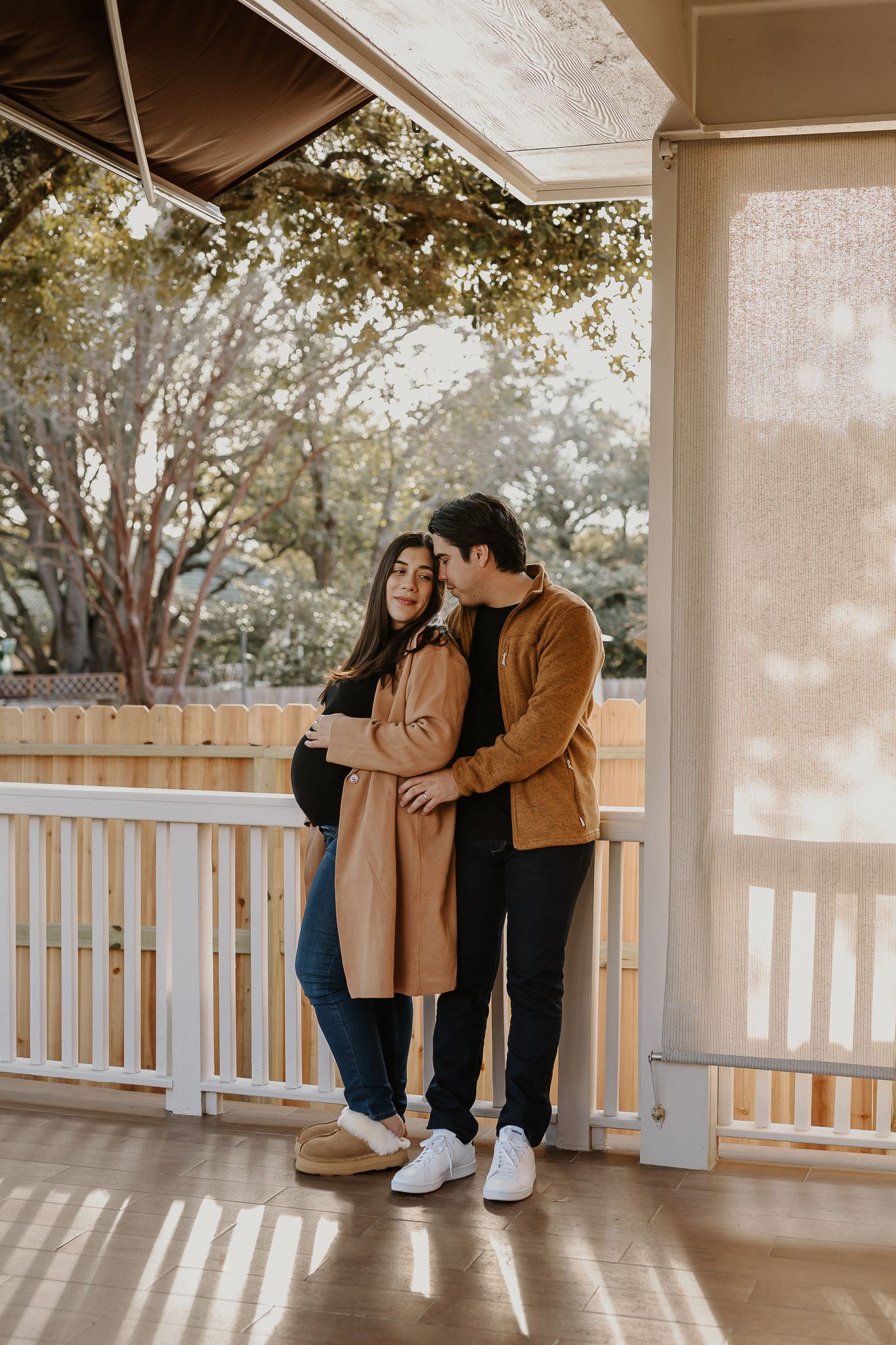 Couple embracing on sunny porch during autumn maternity photoshoot.