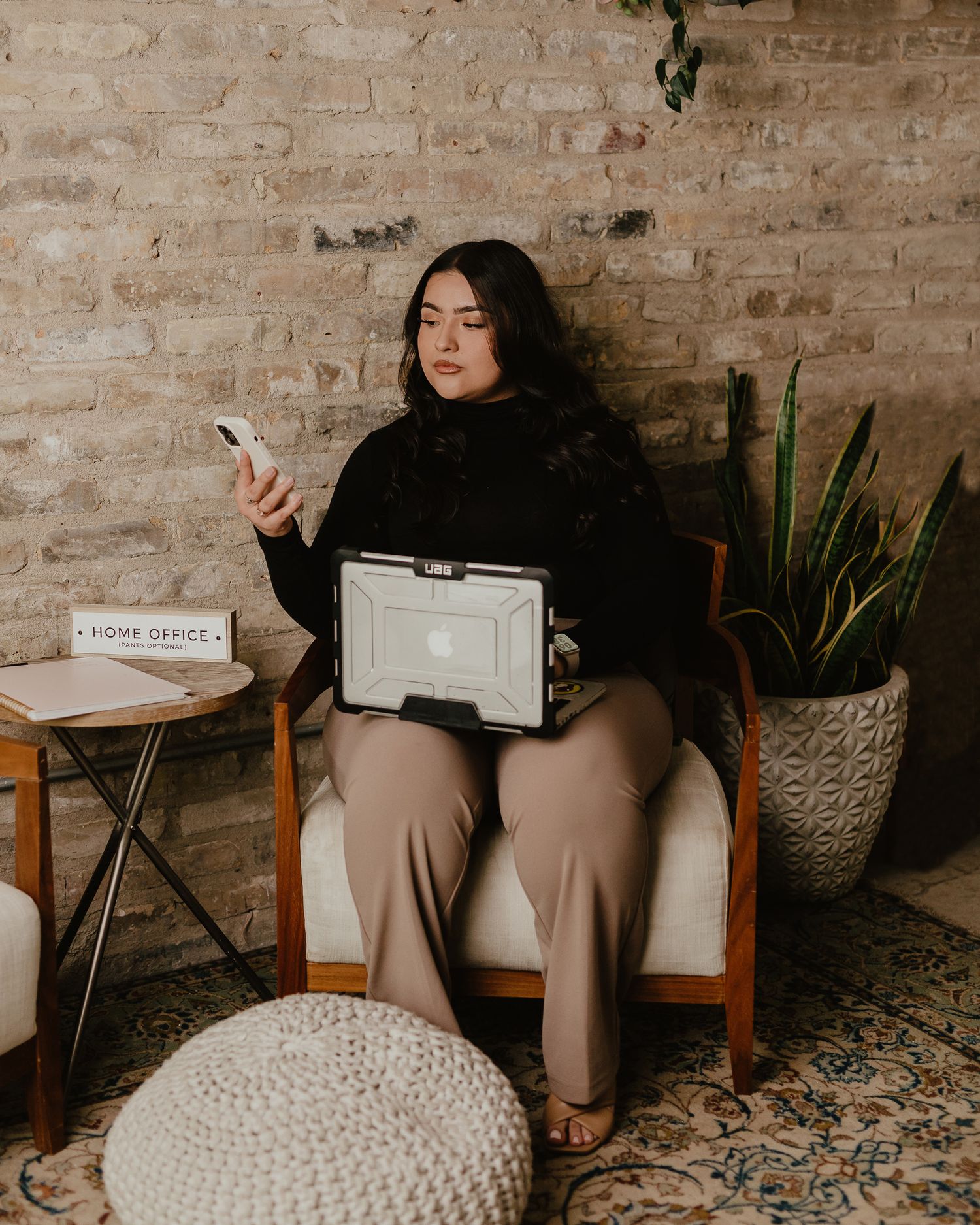 Professional working with phone and laptop in modern office with exposed brick walls.