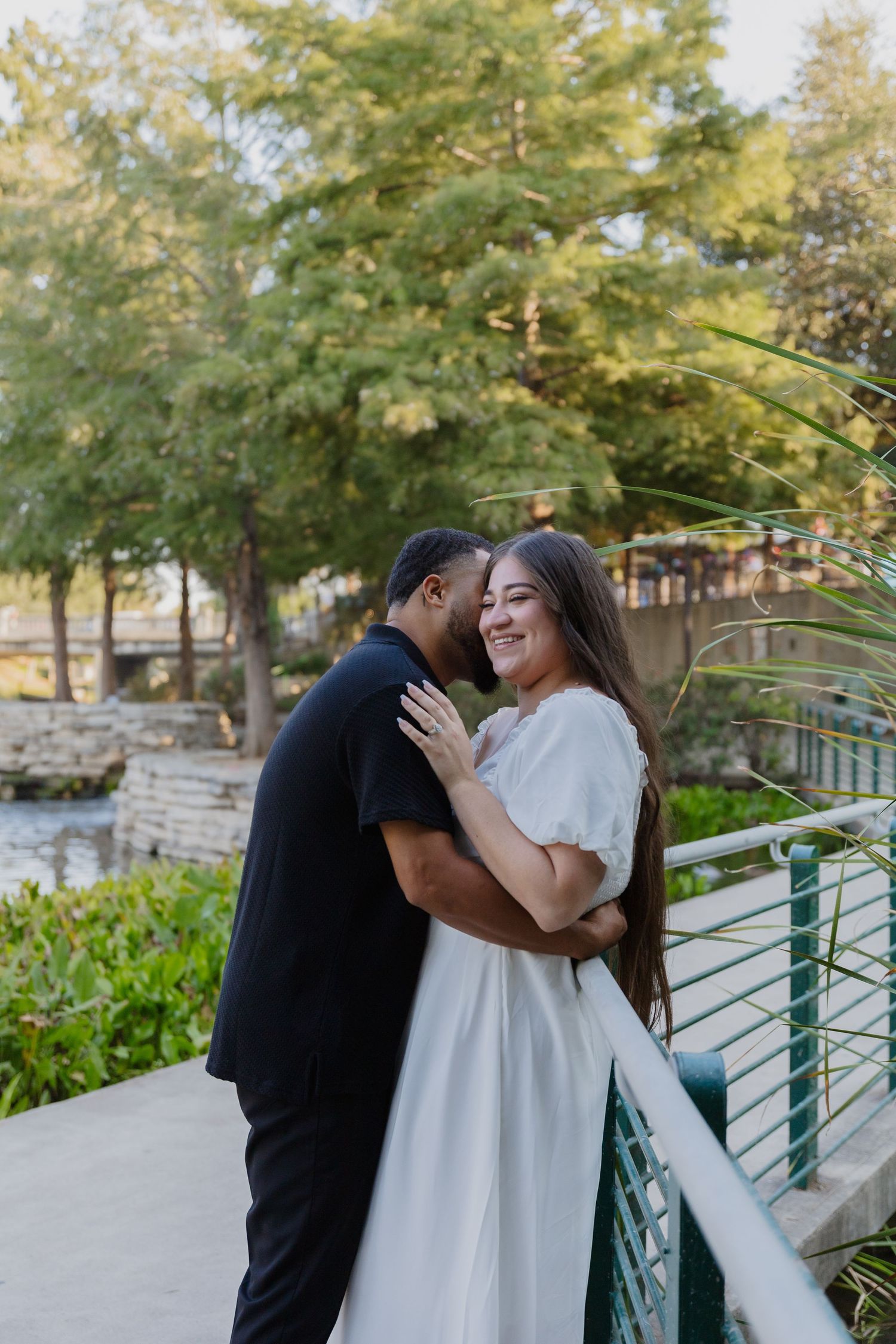 Couple shares joyful moment on white bridge overlooking landscaped garden.