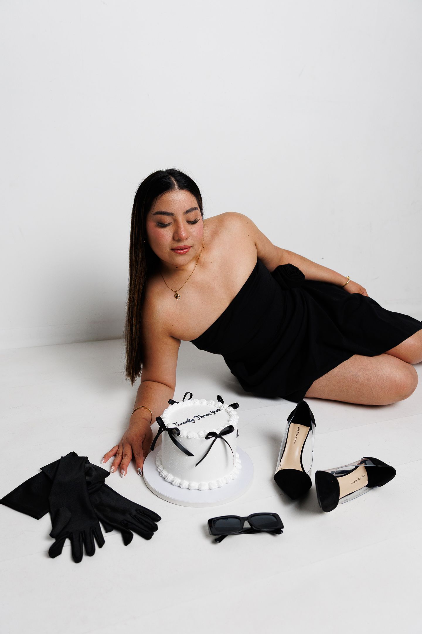 A fashion photoshoot series featuring someone in a black dress posing elegantly with white props and black gloves on a light backdrop.