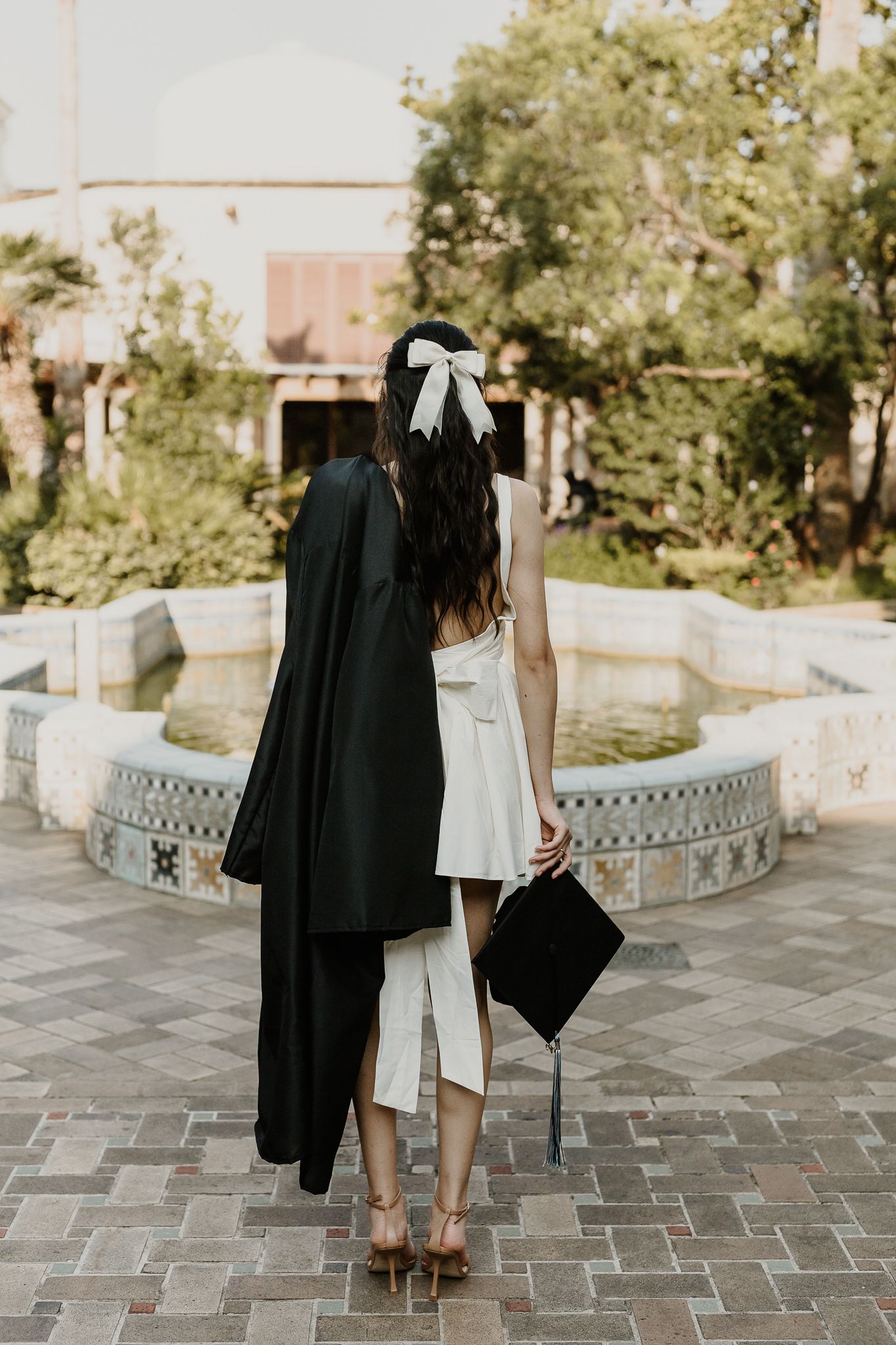 Graduate in black gown and white dress walking with diploma holder.