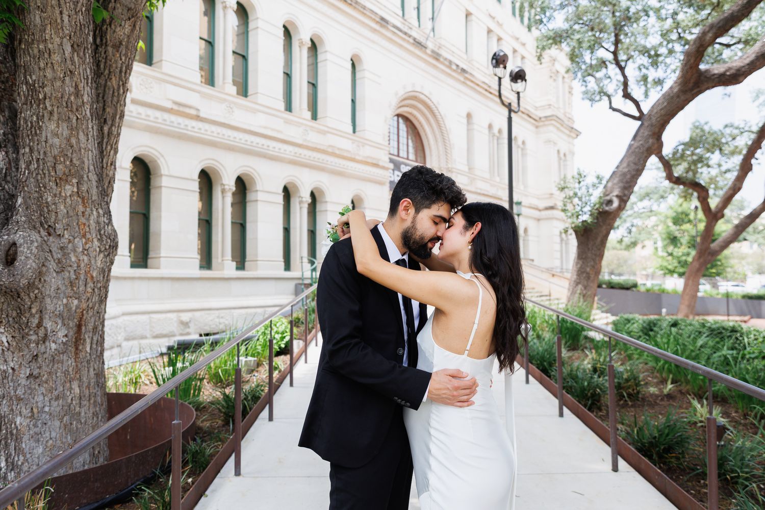 Newlywed couple sharing a romantic kiss outside a historic building on their wedding day.