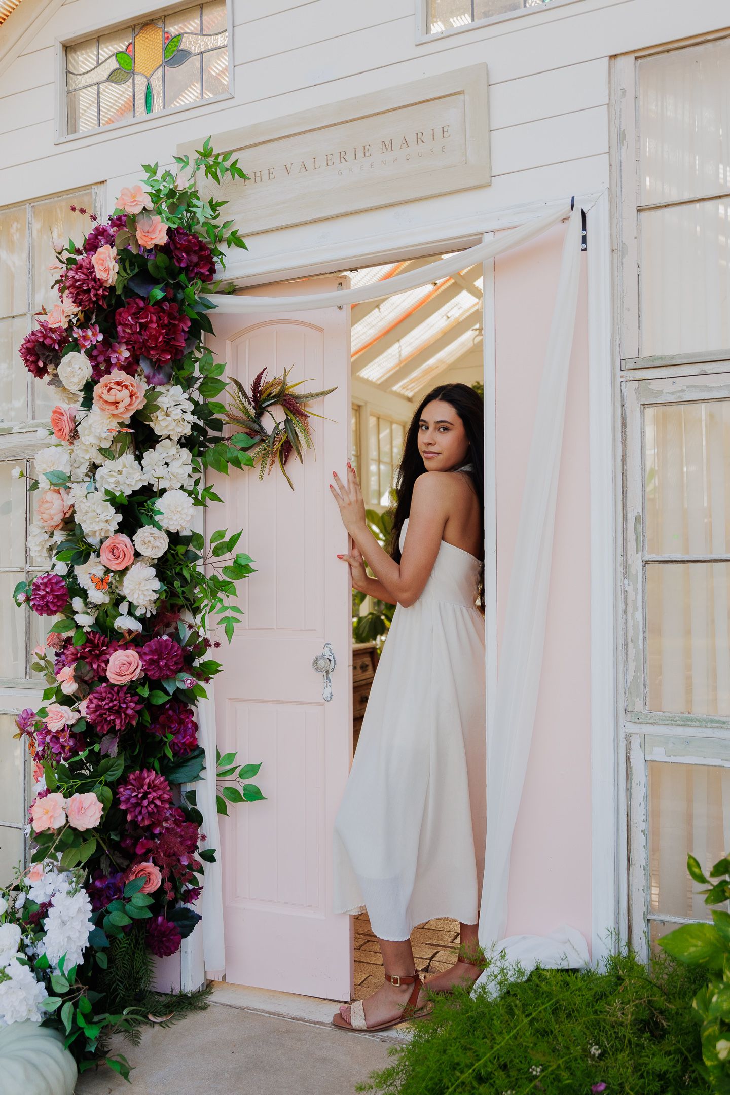 Elegant white door entrance adorned with cascading burgundy and pink floral arrangements and lush greenery.