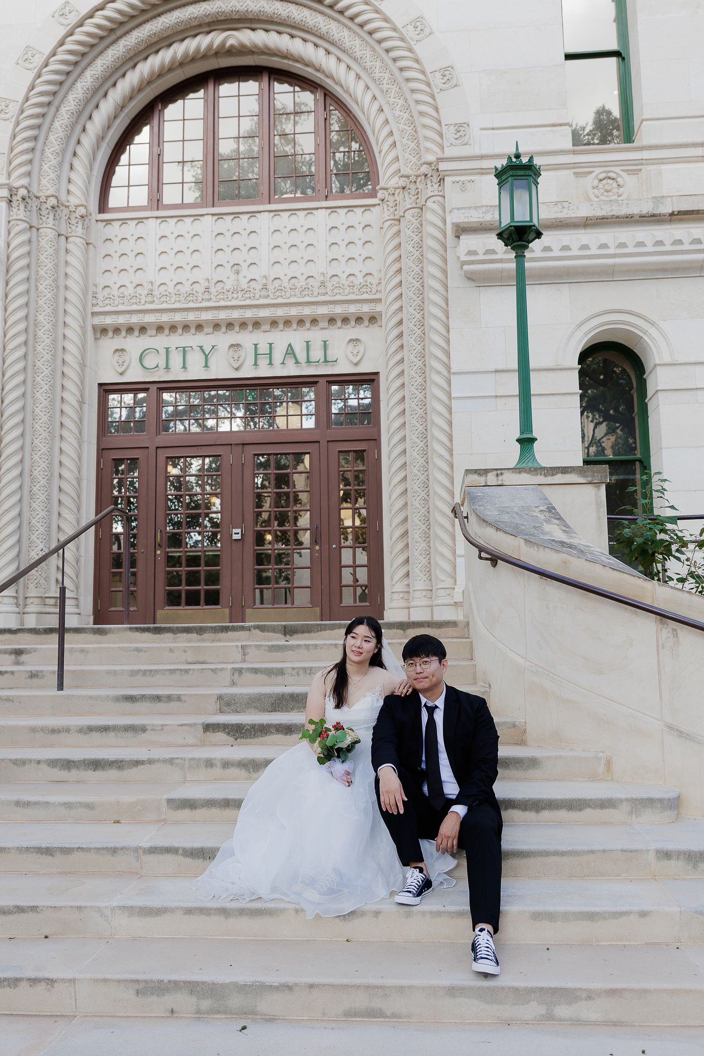 Wedding couple poses playfully on the grand steps of City Hall with classic architectural details in the background.