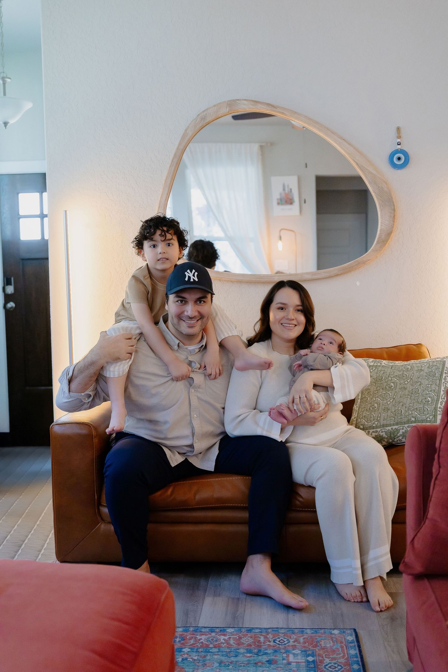 Family relaxing together on brown leather couch in cozy living room with curved mirror and blue accent decor.