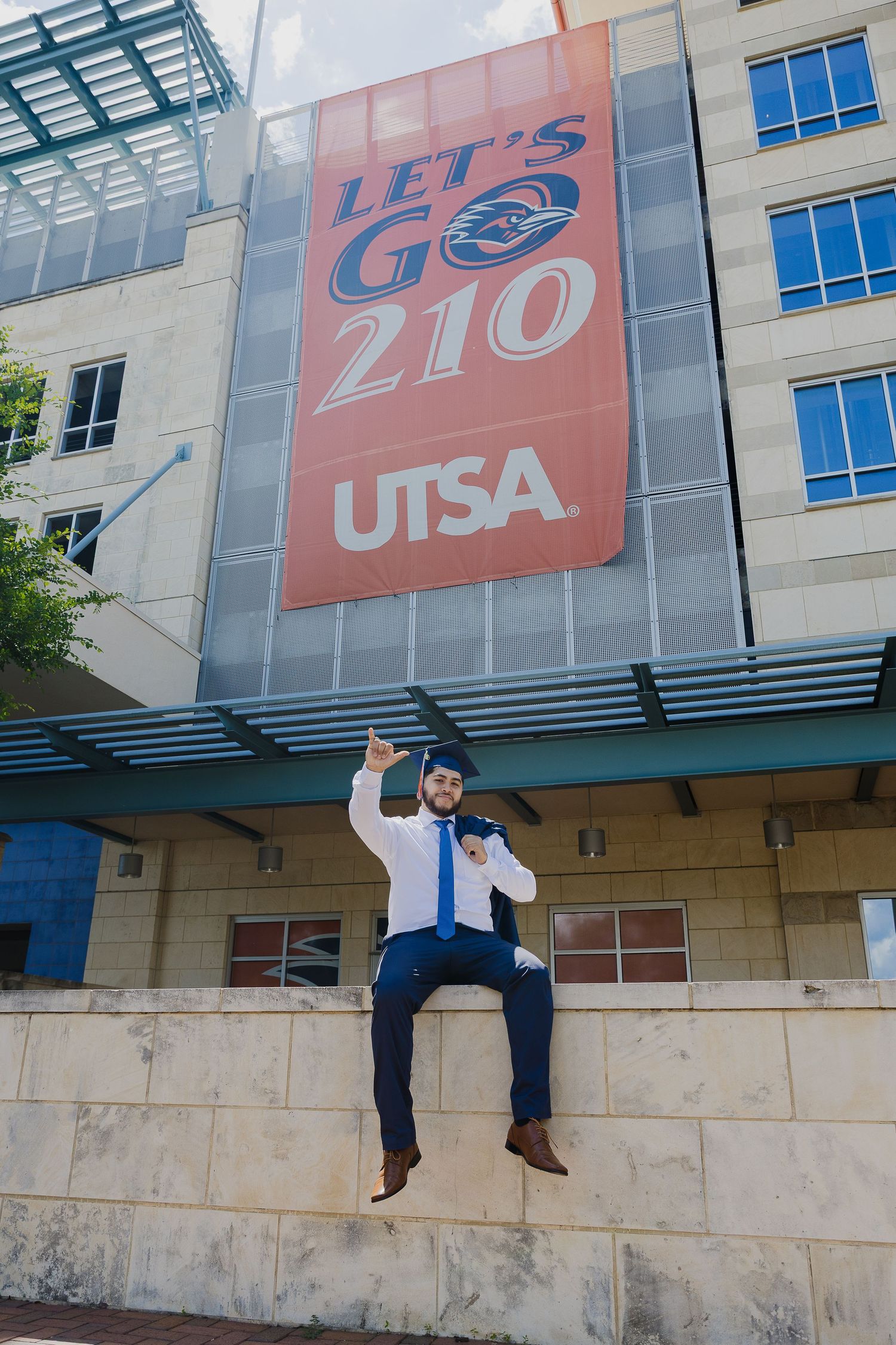 A person in blue jeans sits on a concrete ledge outside a building with large commercial signage above.