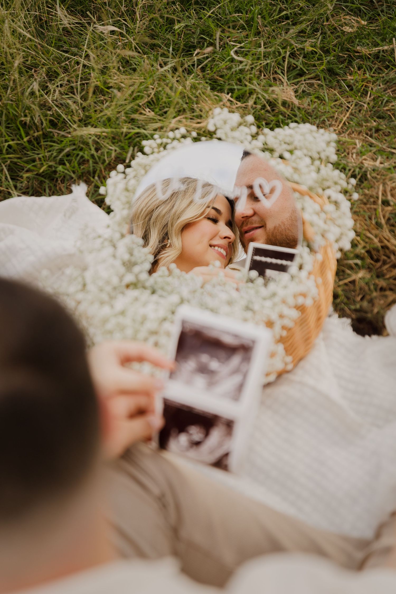 Romantic pregnancy announcement photoshoot with couple lying among baby's breath flowers.